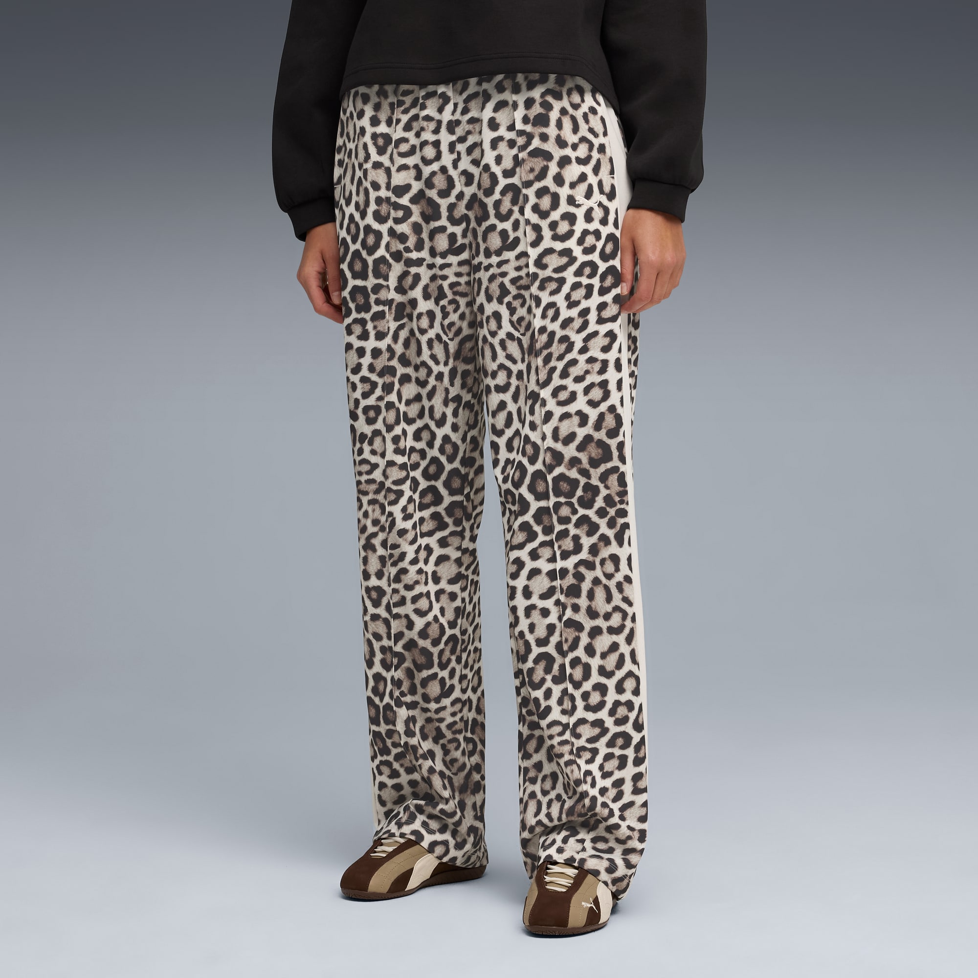 Un modèle sur fond gris présente un pantalon imprimé animal, haut foncé et baskets marron.