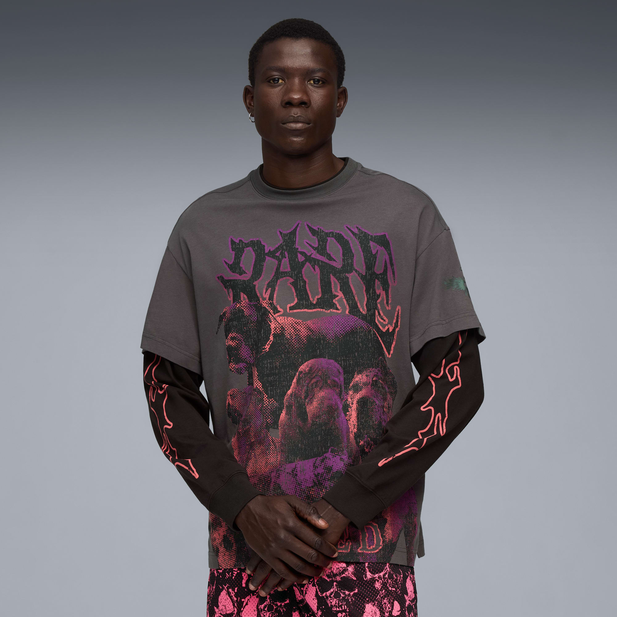 Een model poseert tegen grijs, gekleed in een grafisch T-shirt, top met lange mouwen en een short met print.
