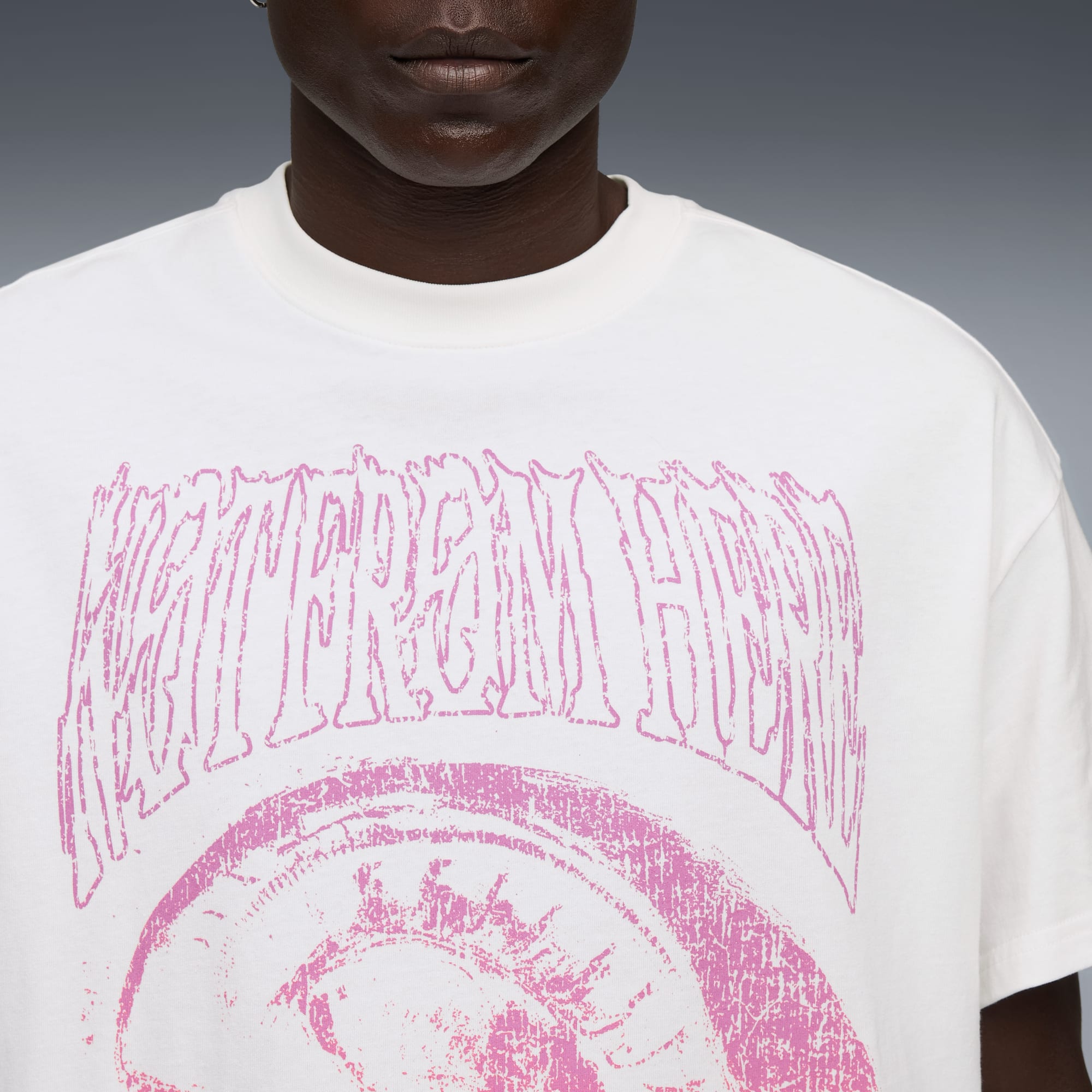 Un modelo lleva una camiseta blanca con un estampado gráfico rosa sobre un fondo gris.