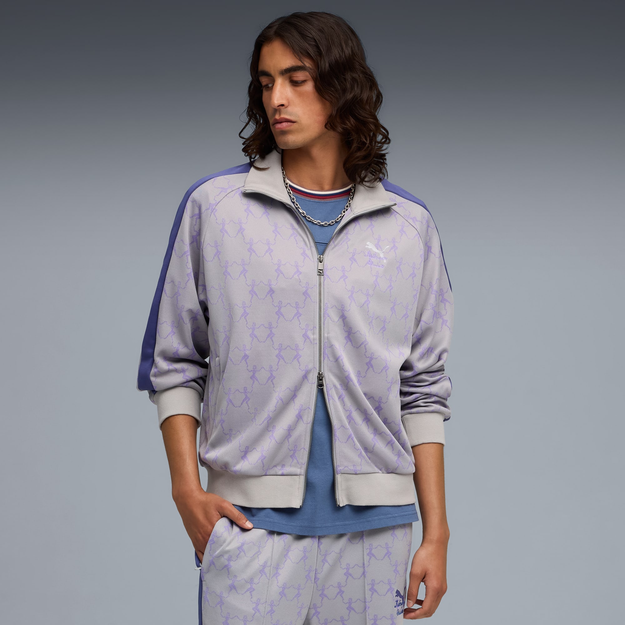 Sobre un fondo gris, un modelo posa con una chaqueta con cremallera estampada y pantalón a juego.