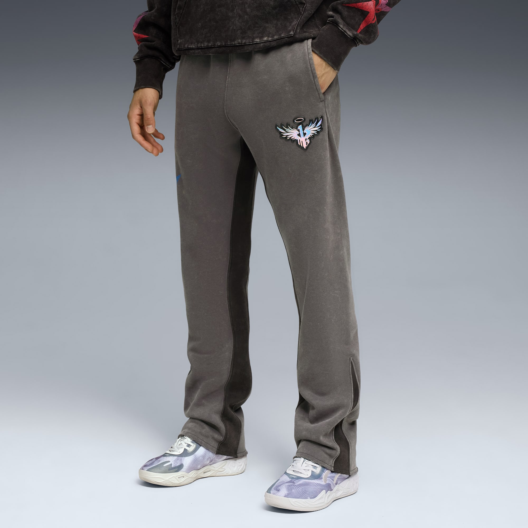 Su uno sfondo grigio, un modello posa in pantaloni da tuta grigi con un emblema e scarpe da ginnastica fantasia.
