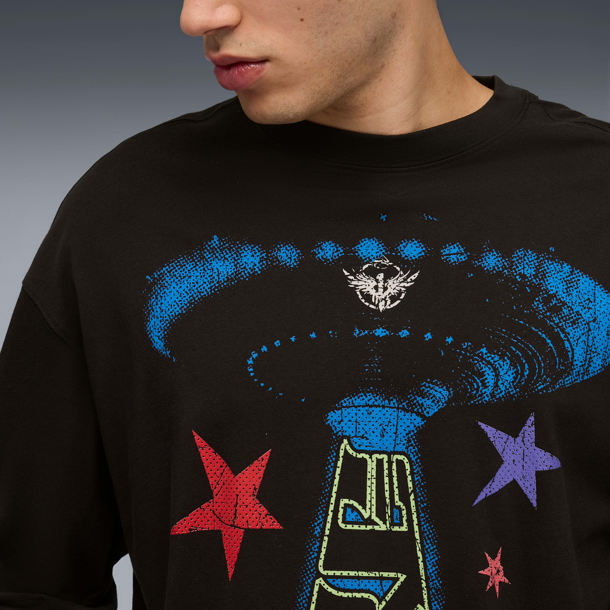 Model ma na sobie czarny top z kolorowym wzorem graficznym na szarym tle.