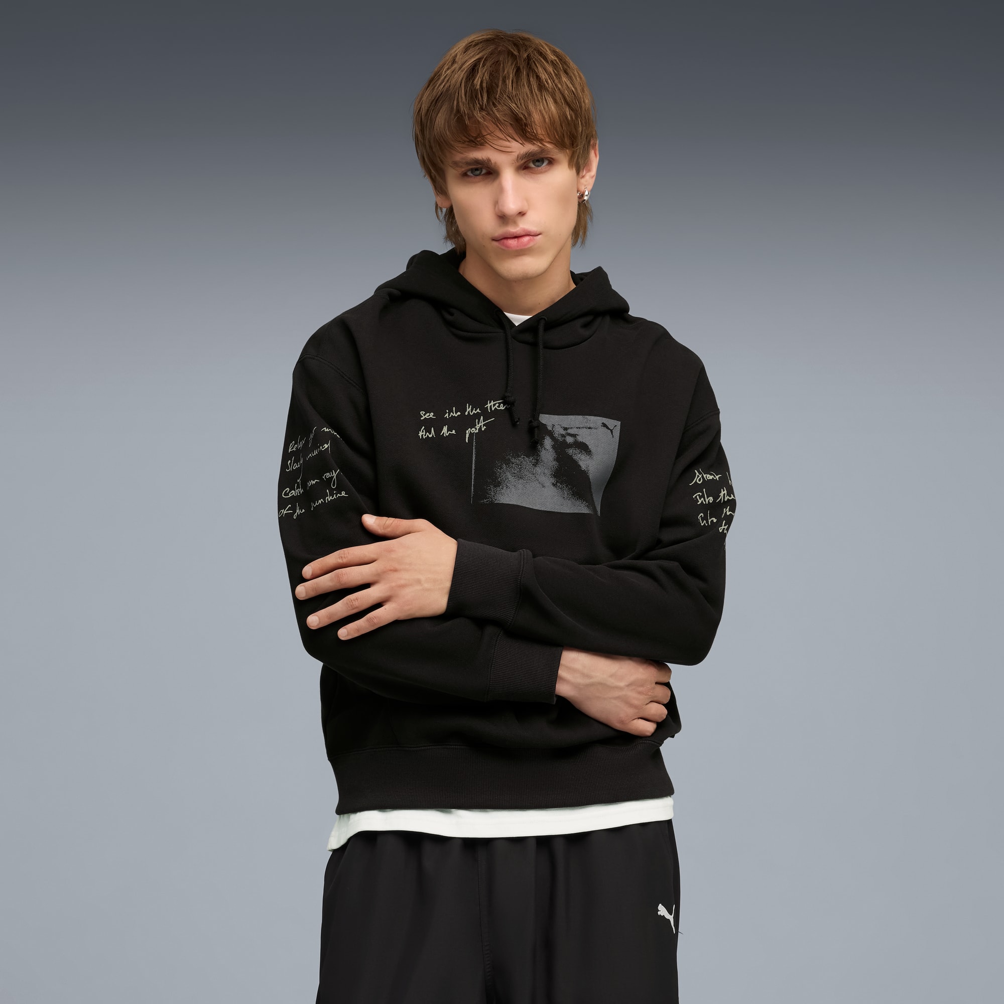 Un modèle pose sur fond gris, portant un sweat à capuche noir imprimé et un short.