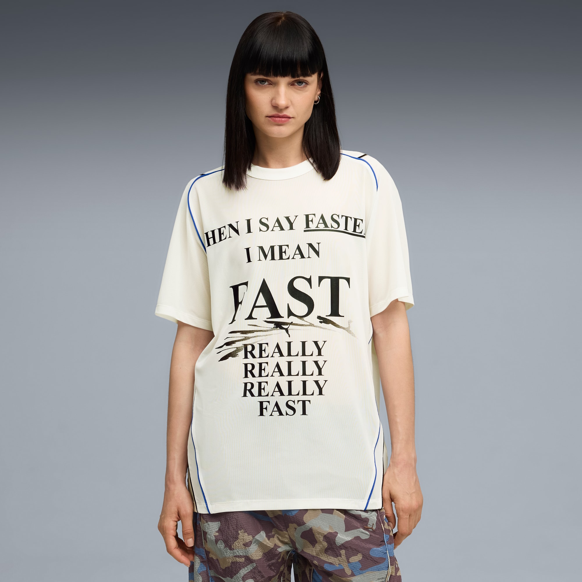 Een model staat tegen een grijze achtergrond, gekleed in een T-shirt met slogan en een short met print.