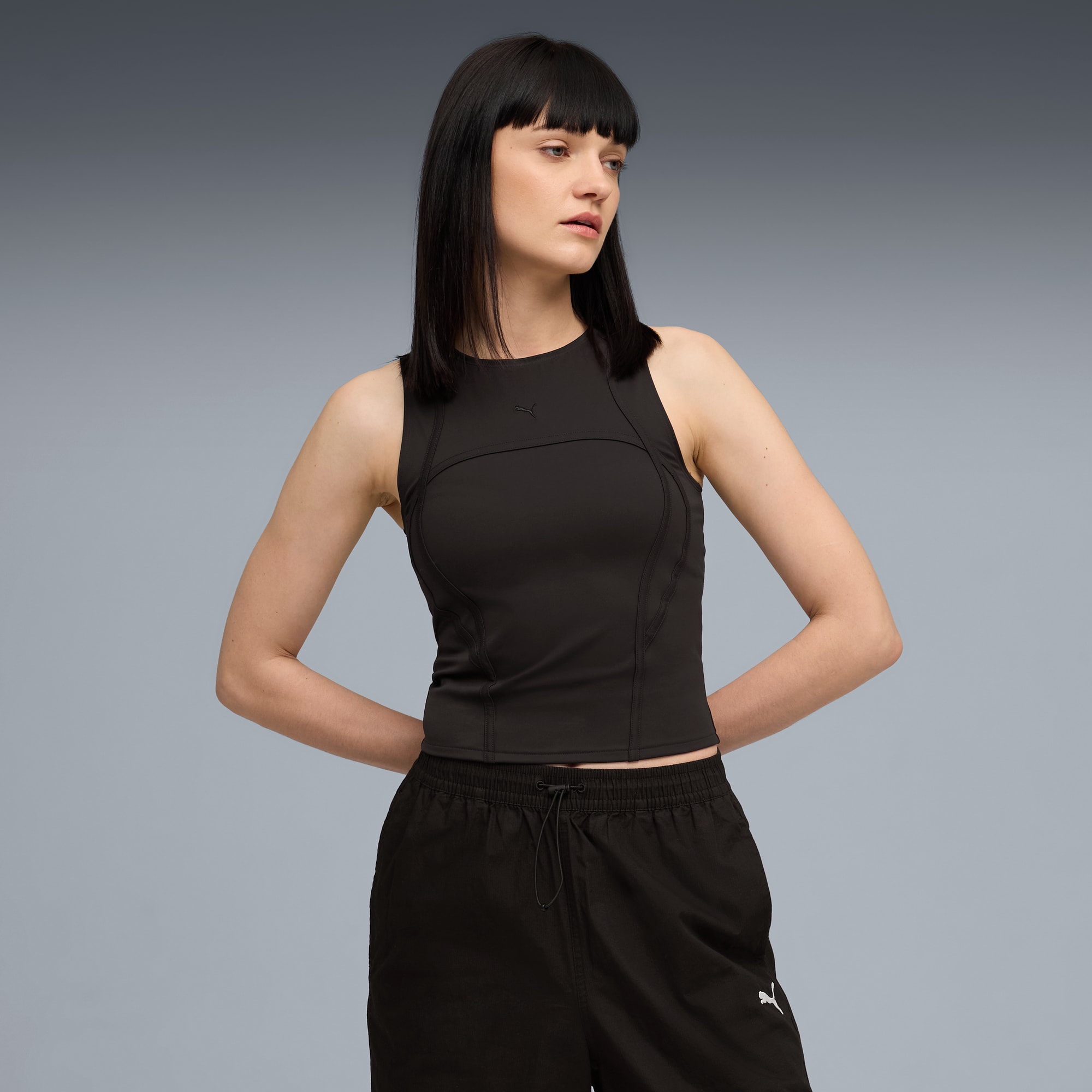 Sobre un fondo gris, una modelo posa con top negro y pantalones cortos deportivos.