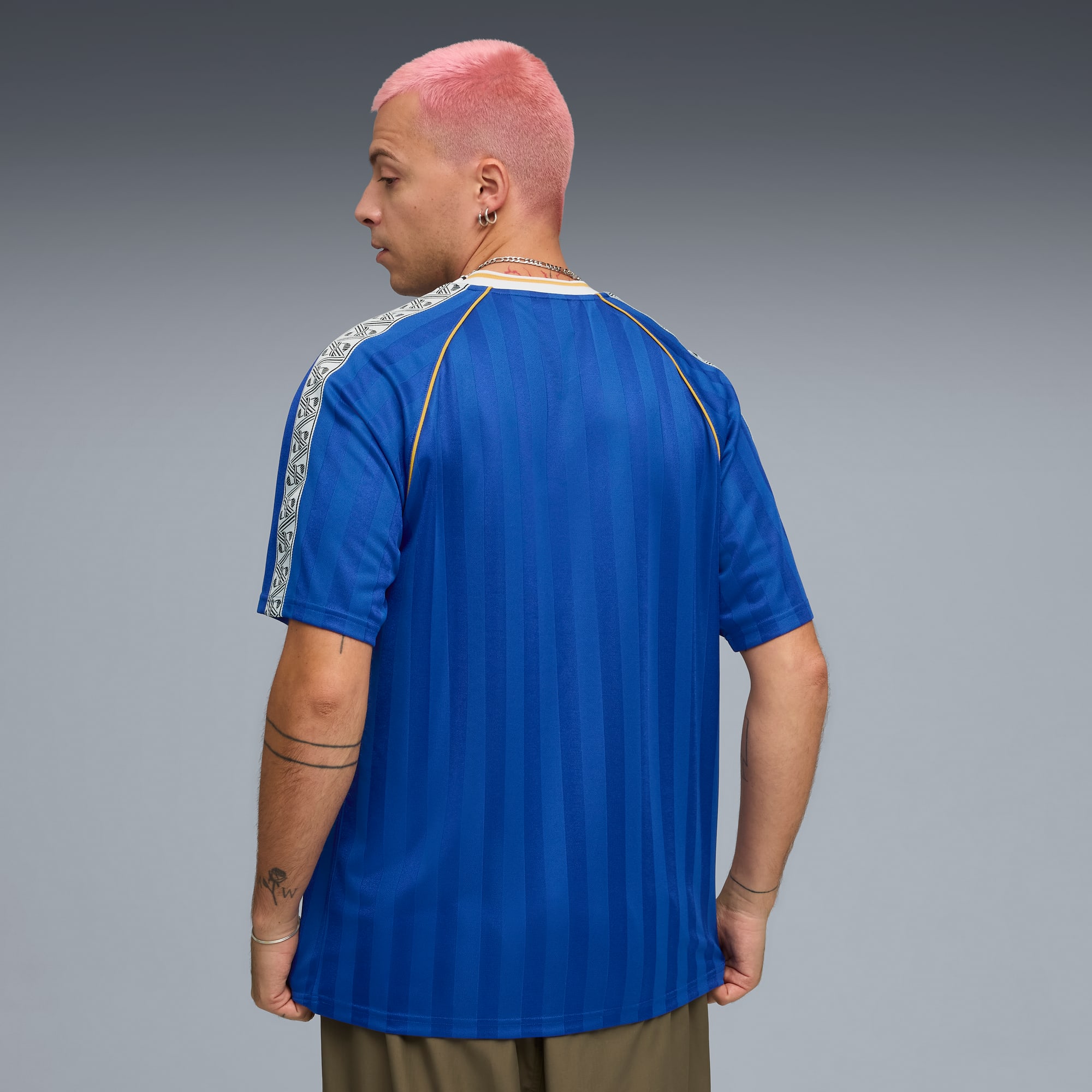 Een model met roze haar poseert tegen een grijze achtergrond, gekleed in een blauw shirt met korte mouwen.