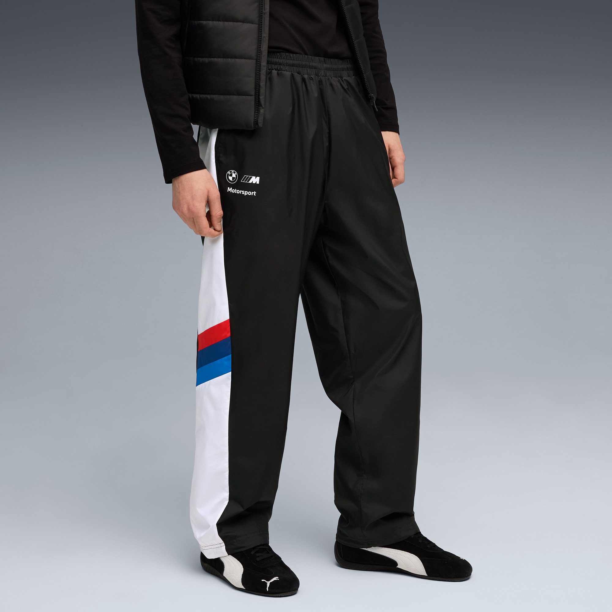 Vor grauem Hintergrund trägt ein Model eine schwarze Hose mit BMW Motorsport-Branding.