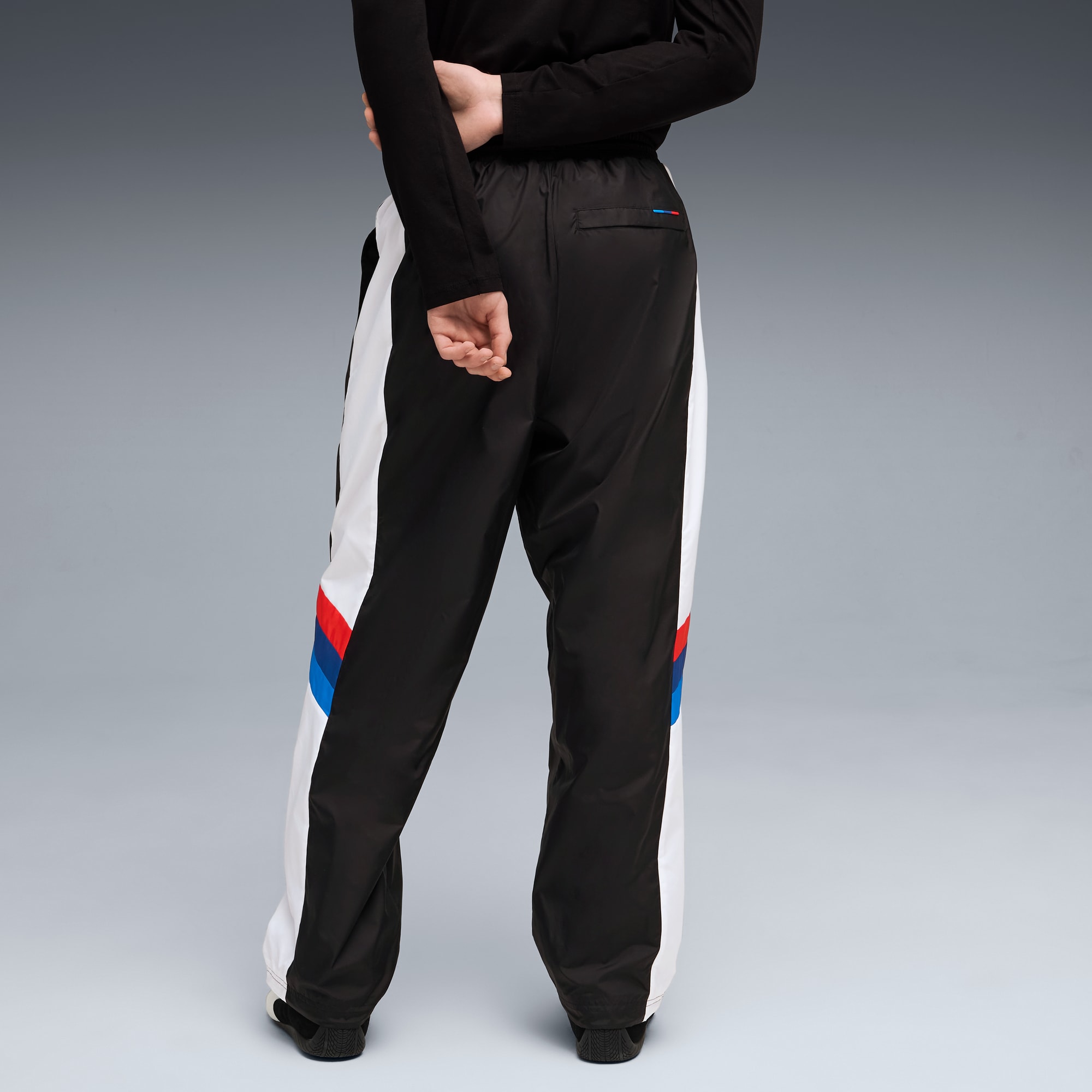 Een model poseert tegen grijs, met zwarte top en zwart-witte broek met kleuraccenten.