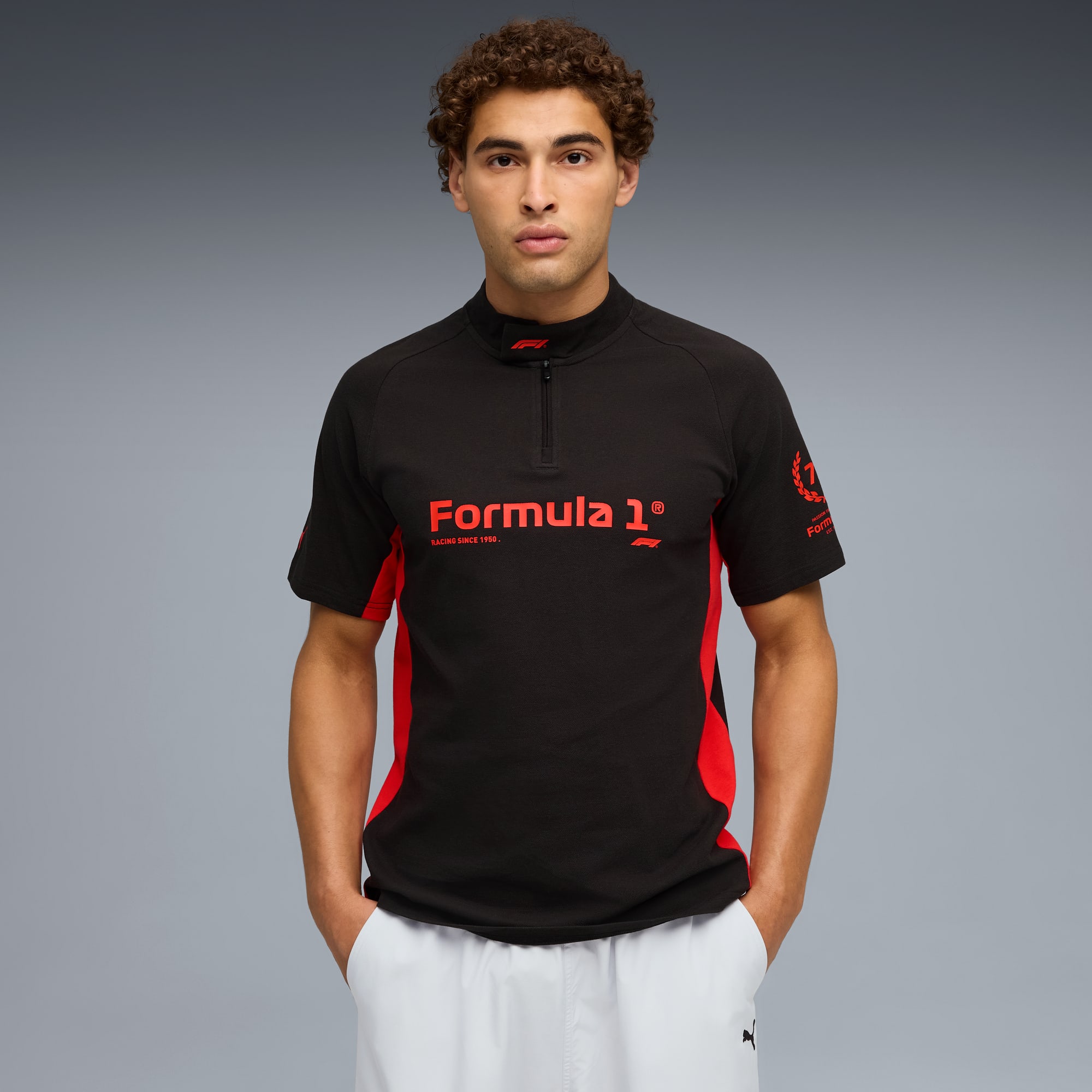 Un modello su sfondo grigio indossa una t-shirt Formula 1 nera e rossa e pantaloncini bianchi.