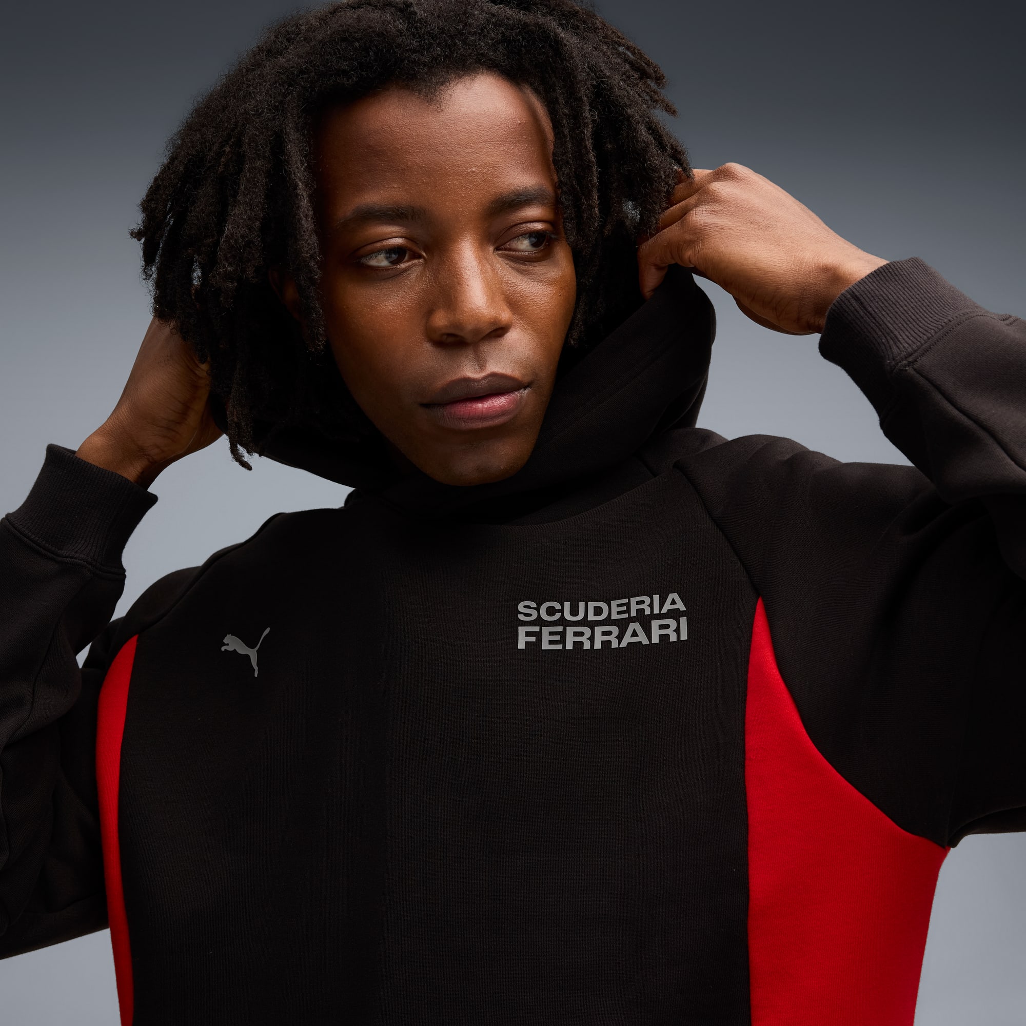 Ein Model vor grauem Hintergrund, das einen schwarzen Scuderia Ferrari Hoodie anpasst.