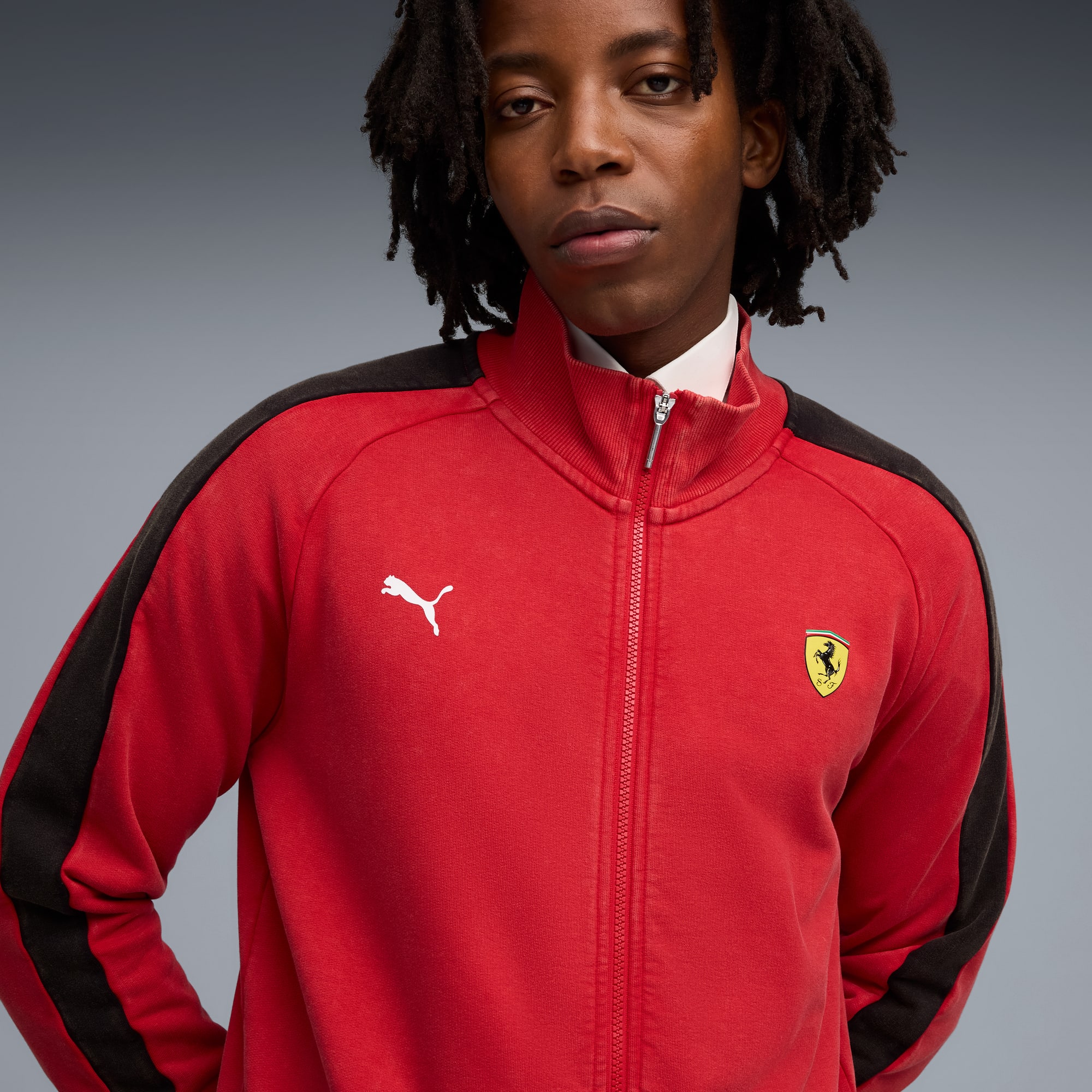 Vor grauem Hintergrund trägt ein Model eine rote Reißverschlussjacke mit Markenlogos.