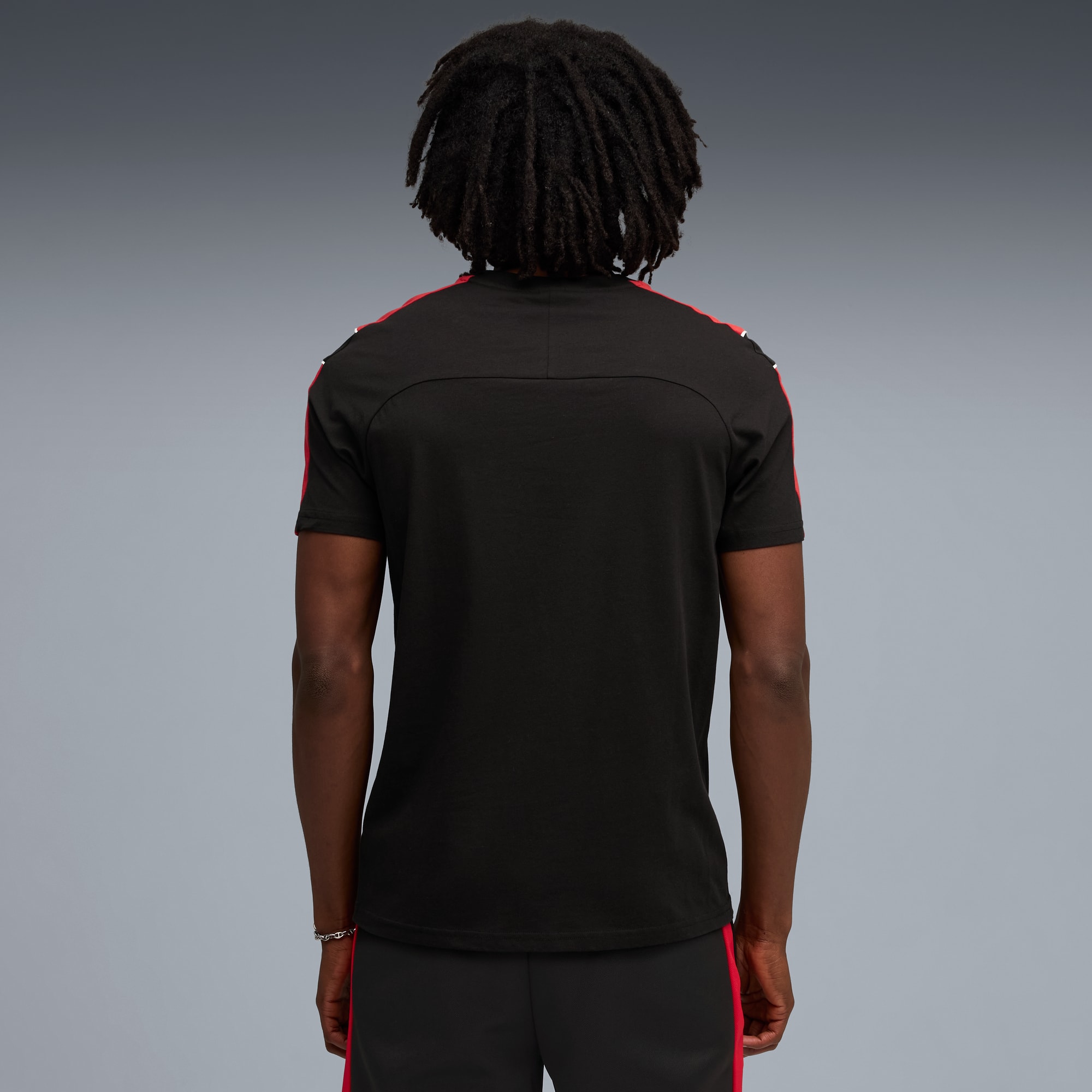 Un modèle, dos à la caméra sur fond gris, porte un t-shirt noir et un short à rayures rouges.