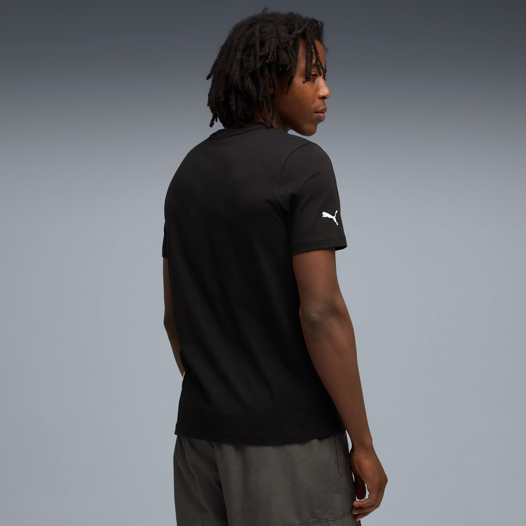 Un modèle regarde à gauche sur fond gris, portant un t-shirt noir et un short gris.