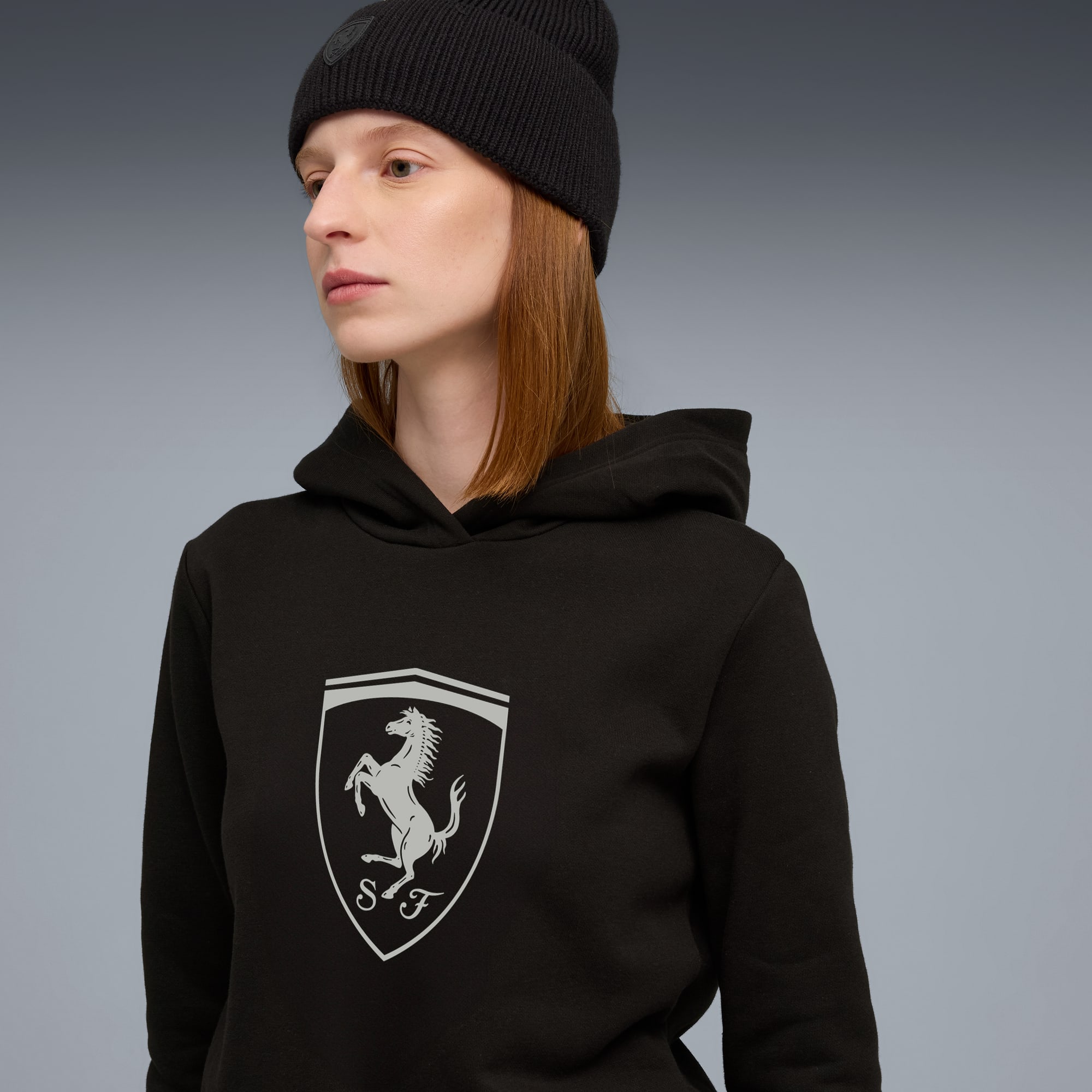 Un mannequin porte un bonnet noir et un sweat à capuche avec un logo sur fond gris.