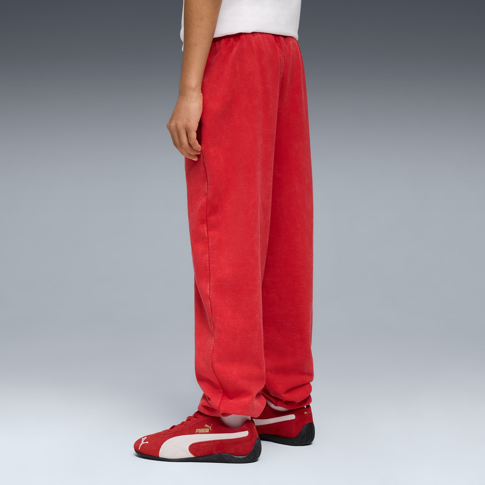 Tegen grijs draagt een model een rode broek, hardloopschoenen en een wit T-shirt.