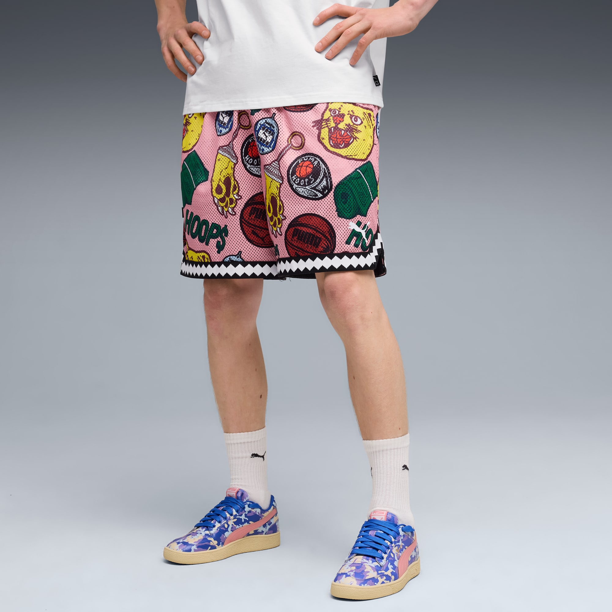 Su sfondo grigio, un modello posa in pantaloncini rosa fantasia, t-shirt e scarpe colorate.