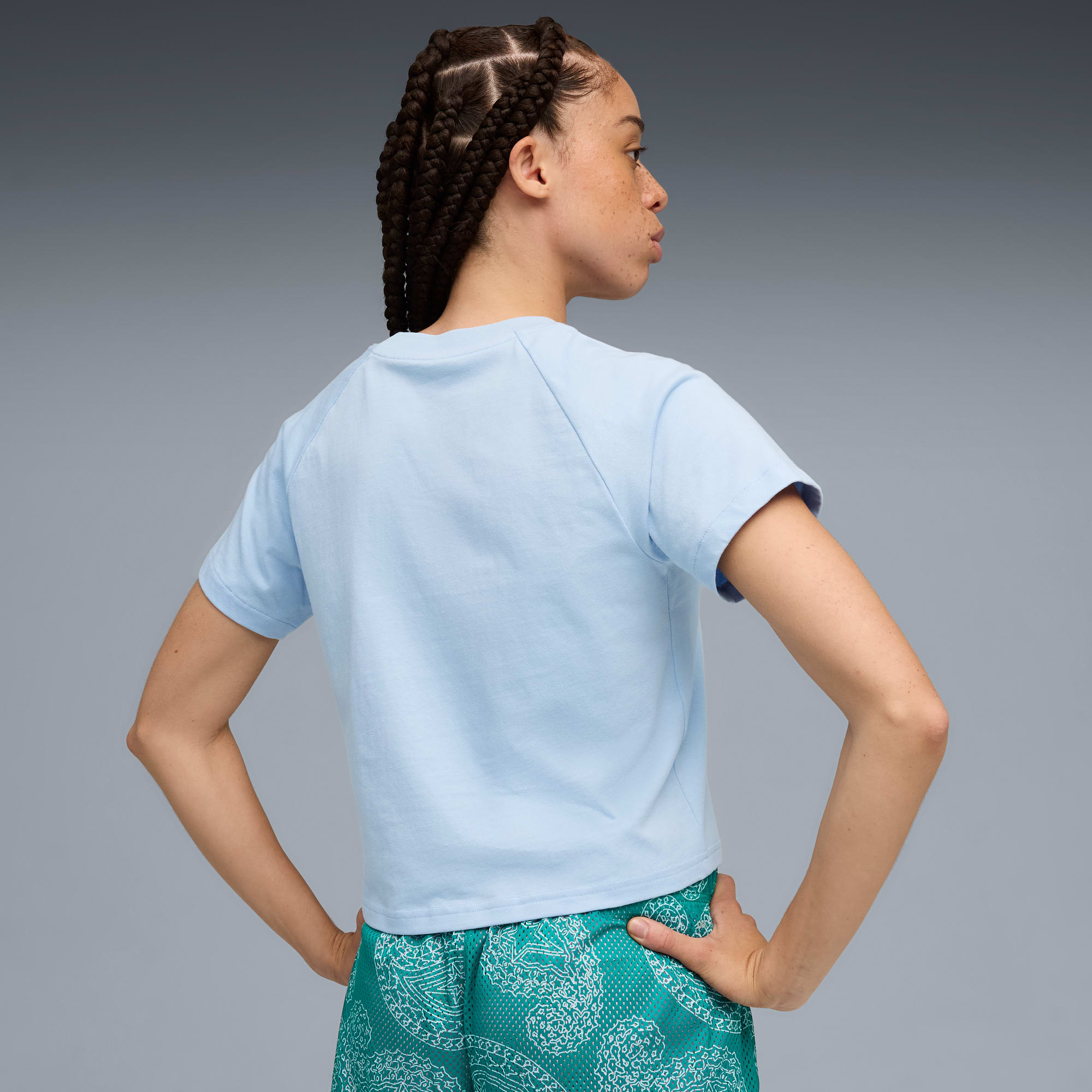 Sobre gris, modelo posa de espaldas, con camiseta azul y pantalón corto verde estampado.