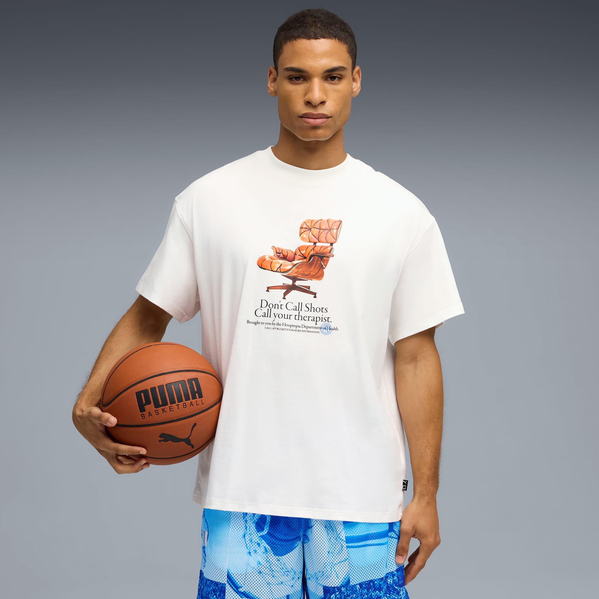 Ein Model posiert mit Basketball vor grauem Hintergrund, trägt bedrucktes T-Shirt und Shorts.