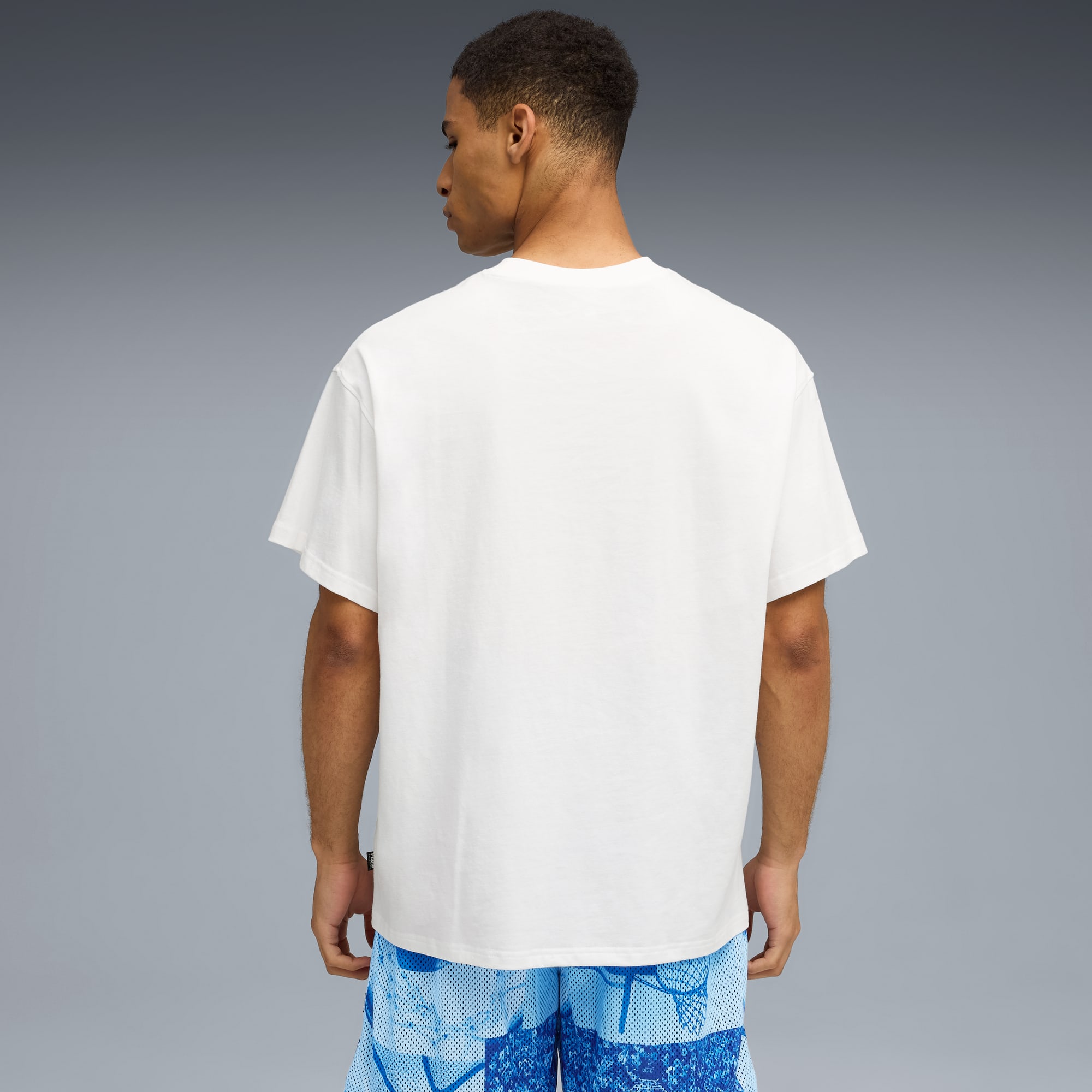 Ein Model mit weißem T-Shirt und gemusterter blauer Shorts steht vor grauem Hintergrund.