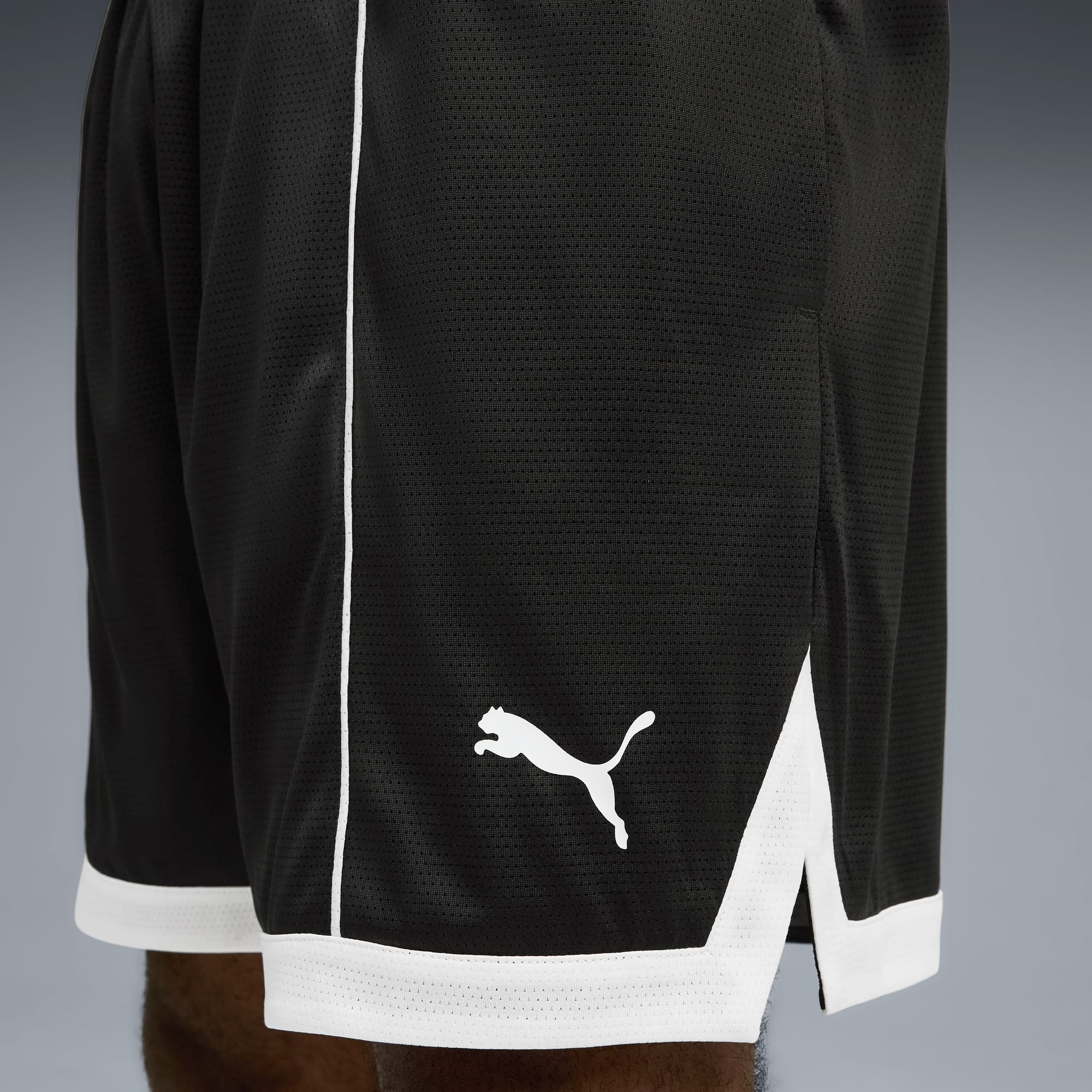 Zbliżenie czarnych spodenek Puma z białym obszyciem i logo na szarym tle.