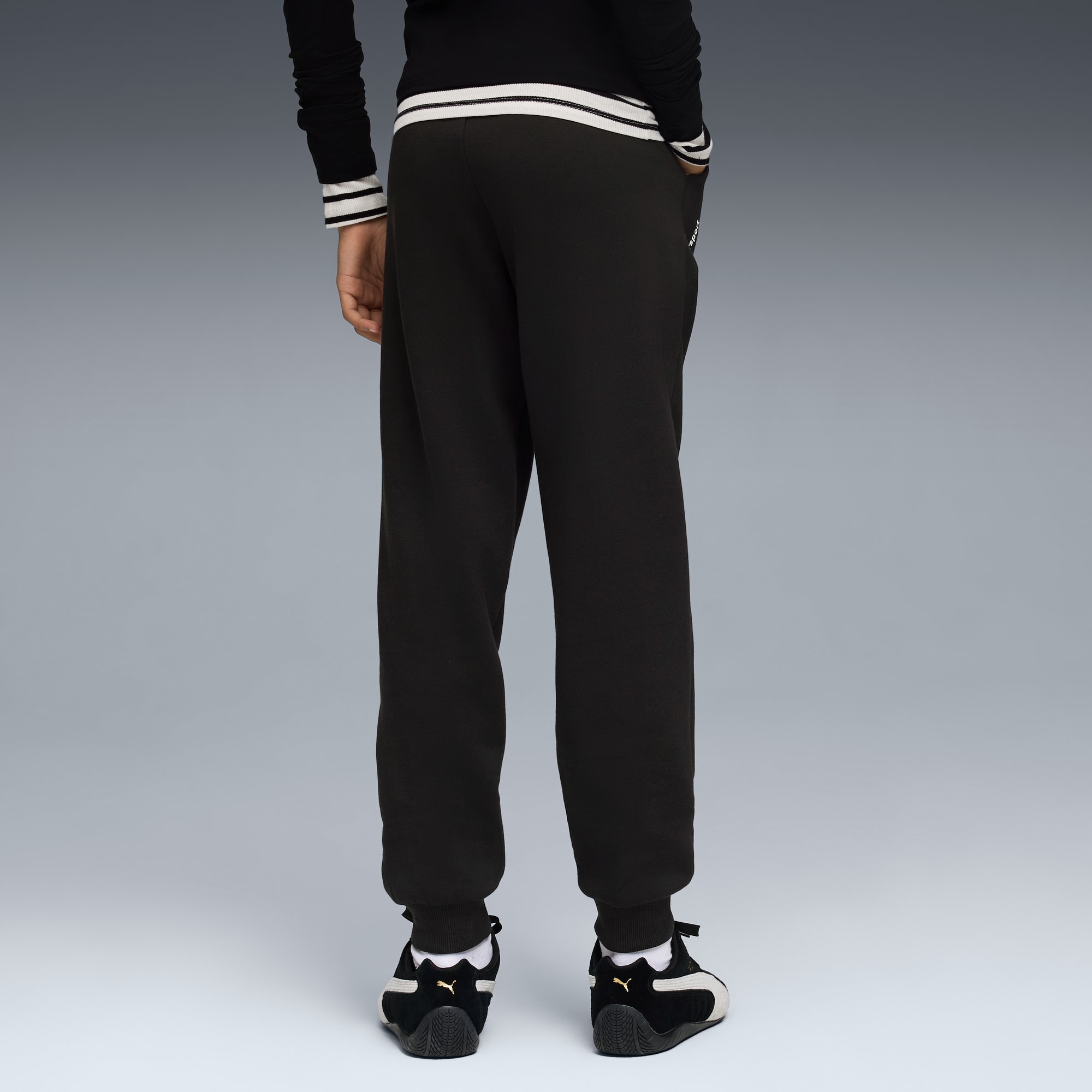 Un modèle de dos sur fond gris porte un jogging noir et des baskets noires et blanches.