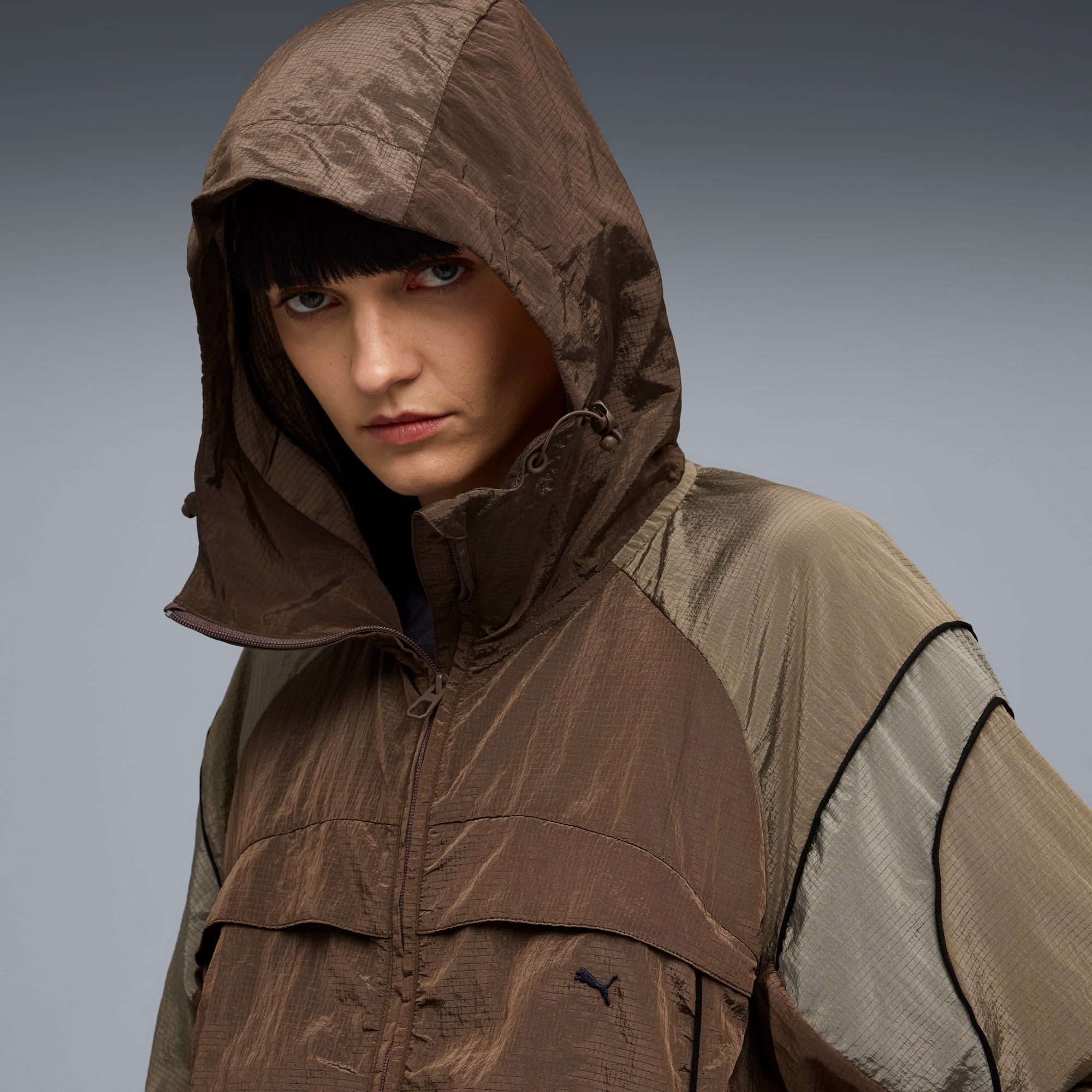 Ein Model vor grauem Hintergrund trägt eine braun-beige Kapuzenjacke.