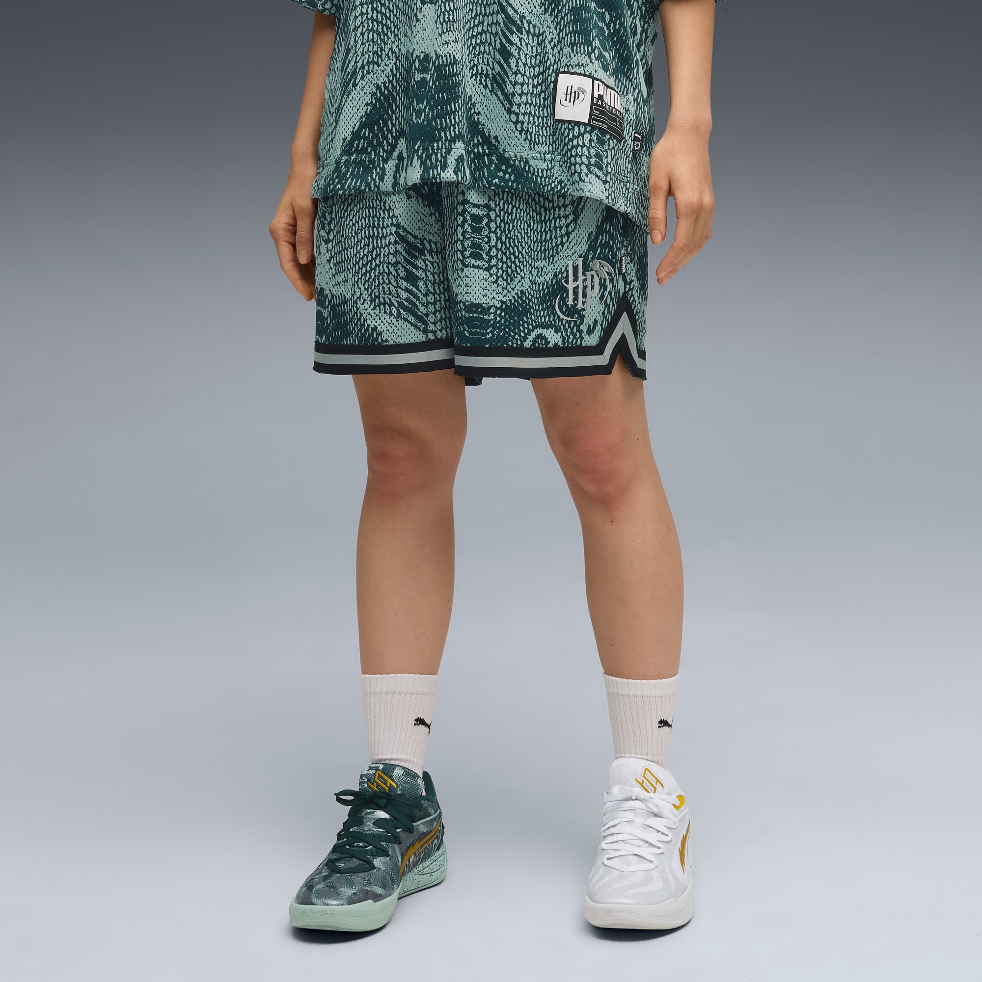 Vor grauem Hintergrund trägt ein Model gemusterte Shorts und unterschiedliche Schuhe.