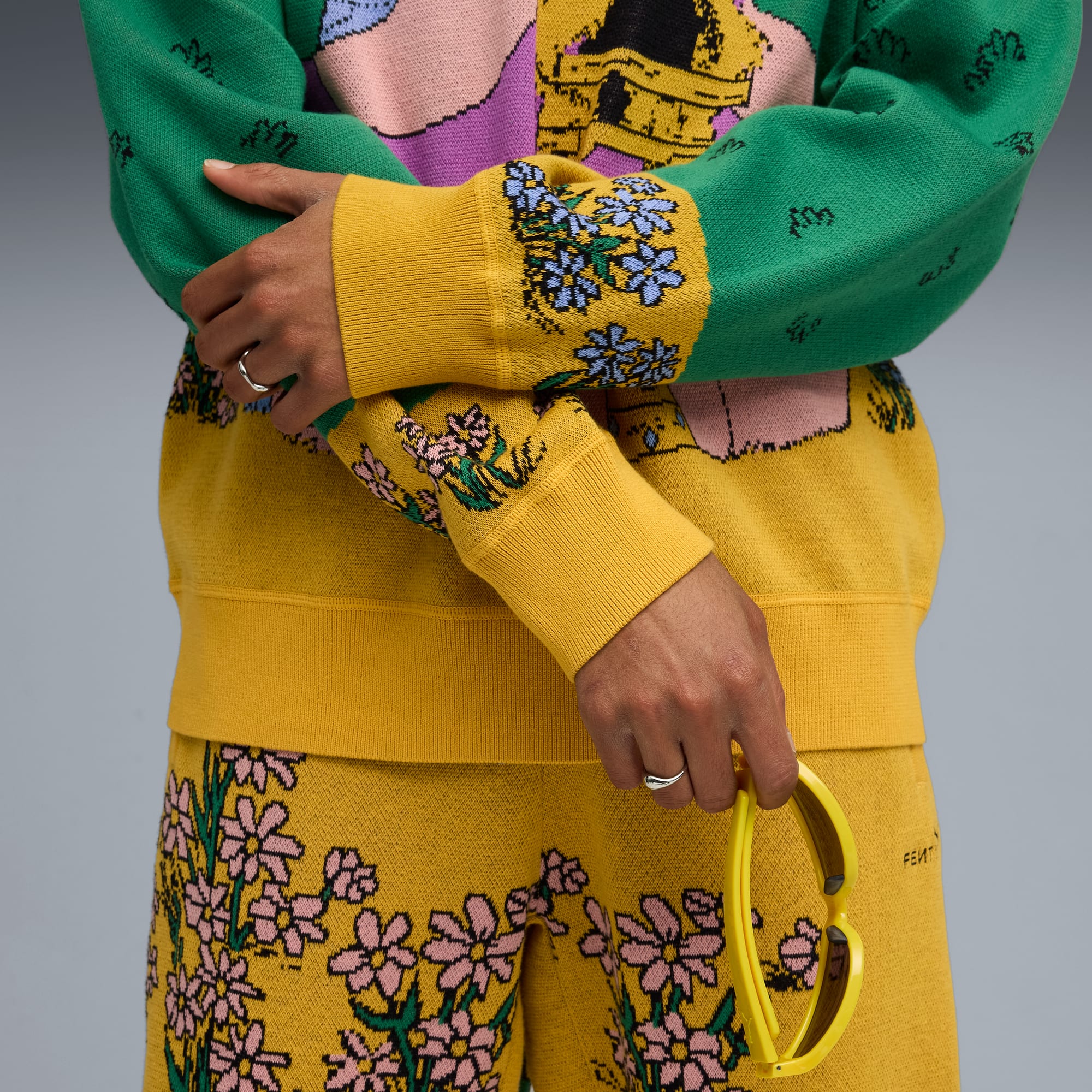 Un mod&egrave;le pose sur fond gris, portant un ensemble en maille &agrave; motifs vert, jaune et rose.