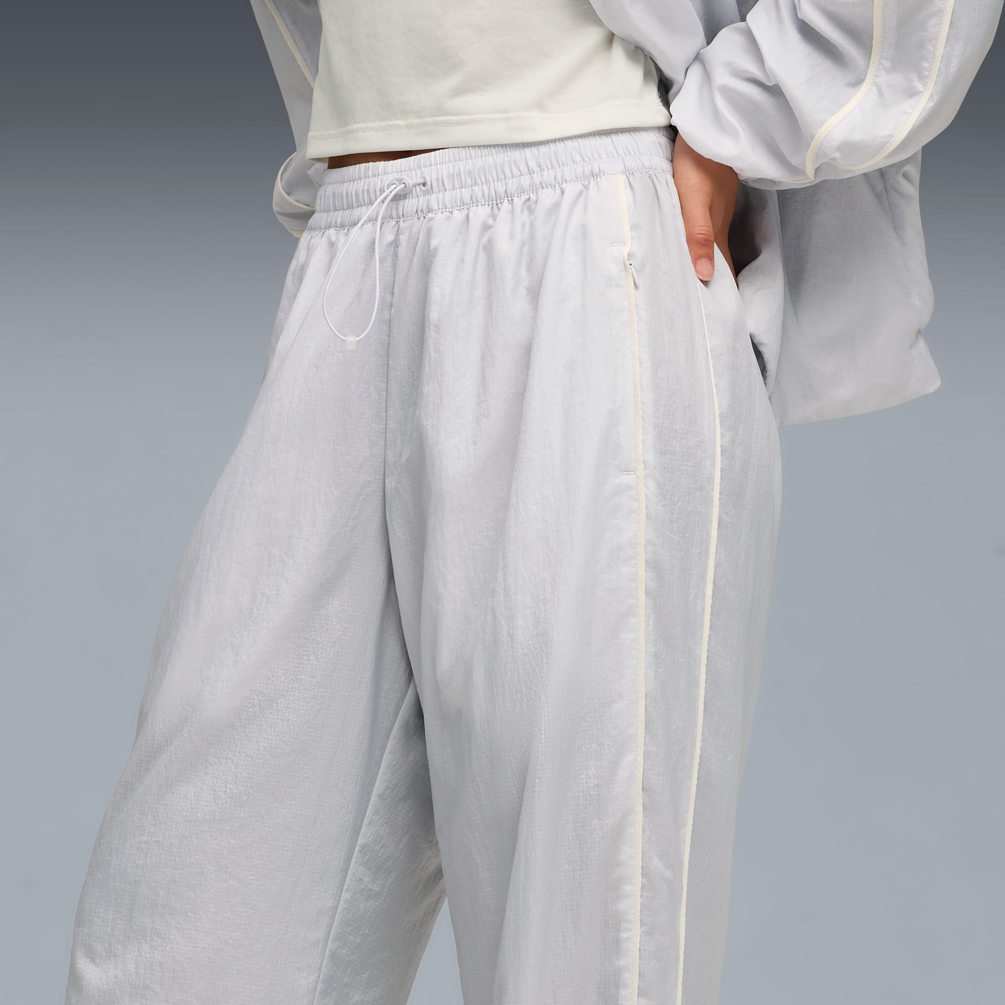 Sur fond gris, un modèle pose en pantalon gris clair à rayures crème et veste assortie.