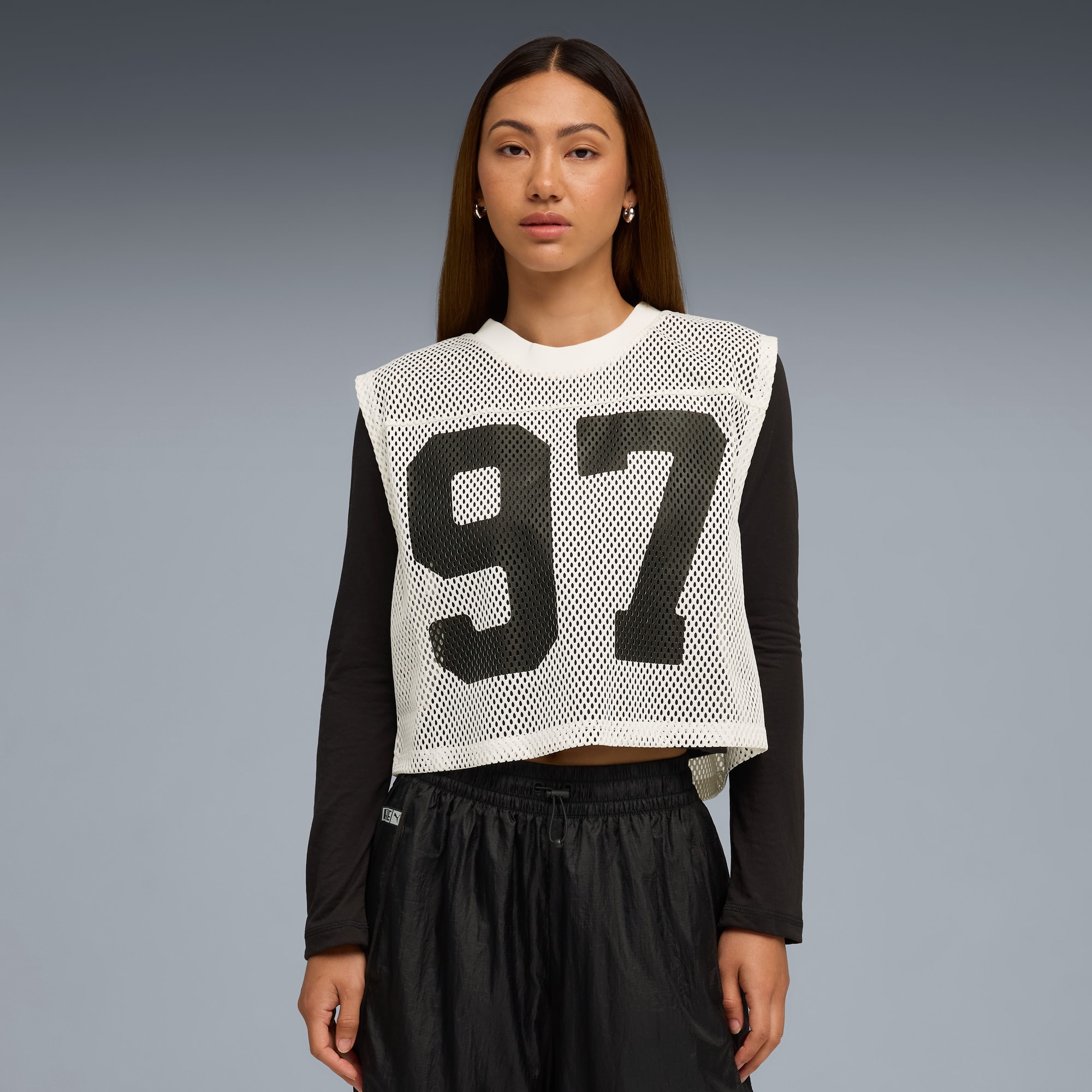 Model posiert vor grauem Hintergrund mit einem '97'-Netztop, schwarzem Langarmshirt und schwarzen Shorts.