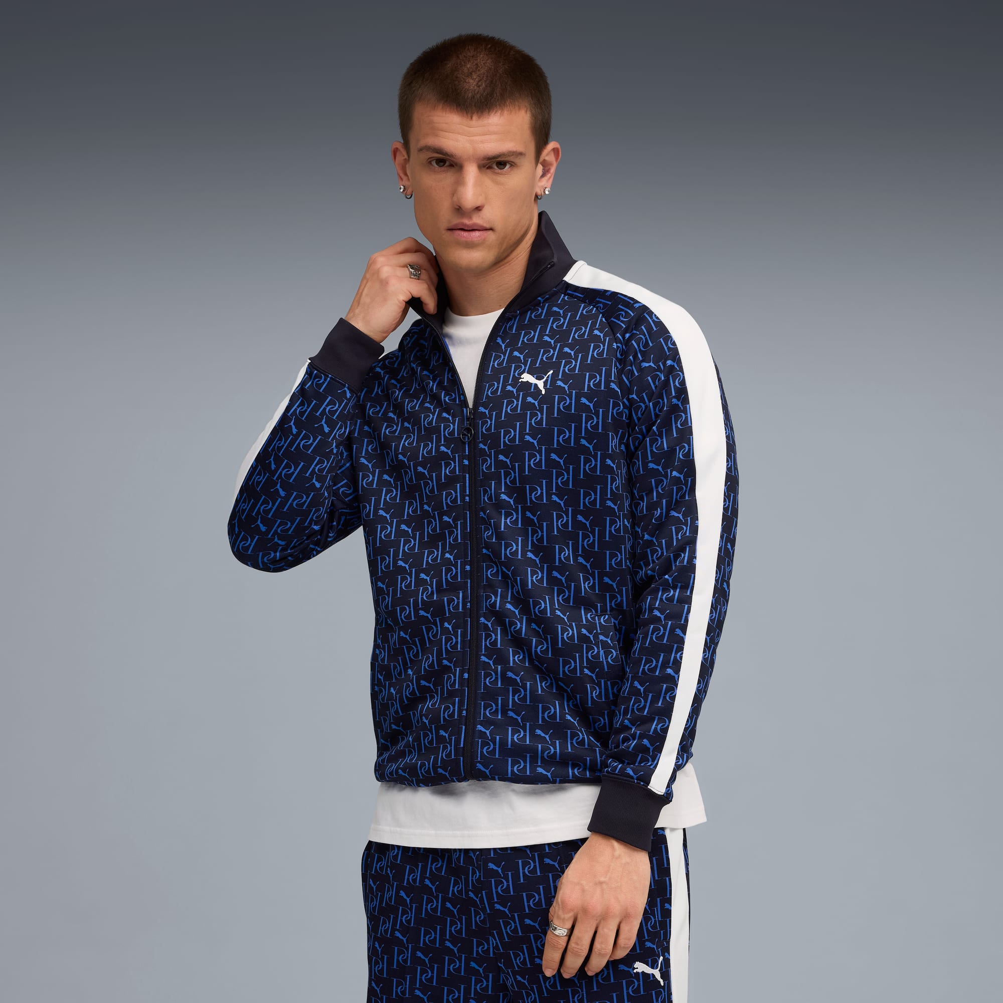 Un mannequin pose sur fond gris, vêtu d'une veste bleue à motifs et d'un pantalon assorti.