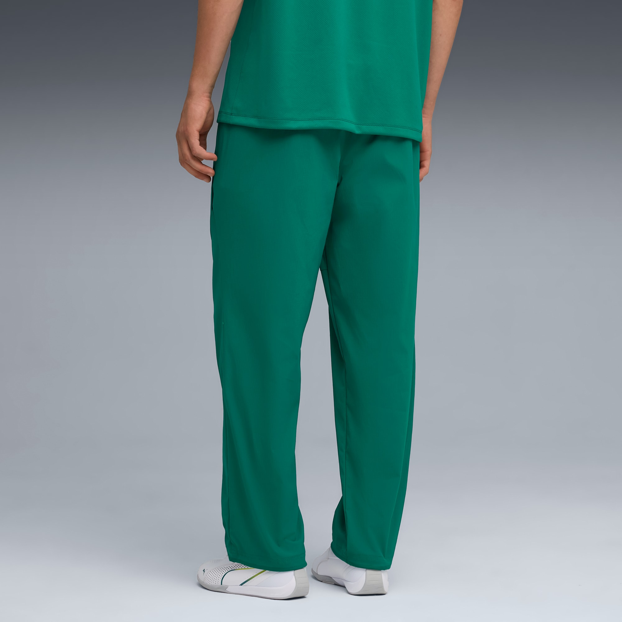 Ein Model steht vor grauem Hintergrund und trägt ein grünes Oberteil, passende Hose und weisse Turnschuhe.