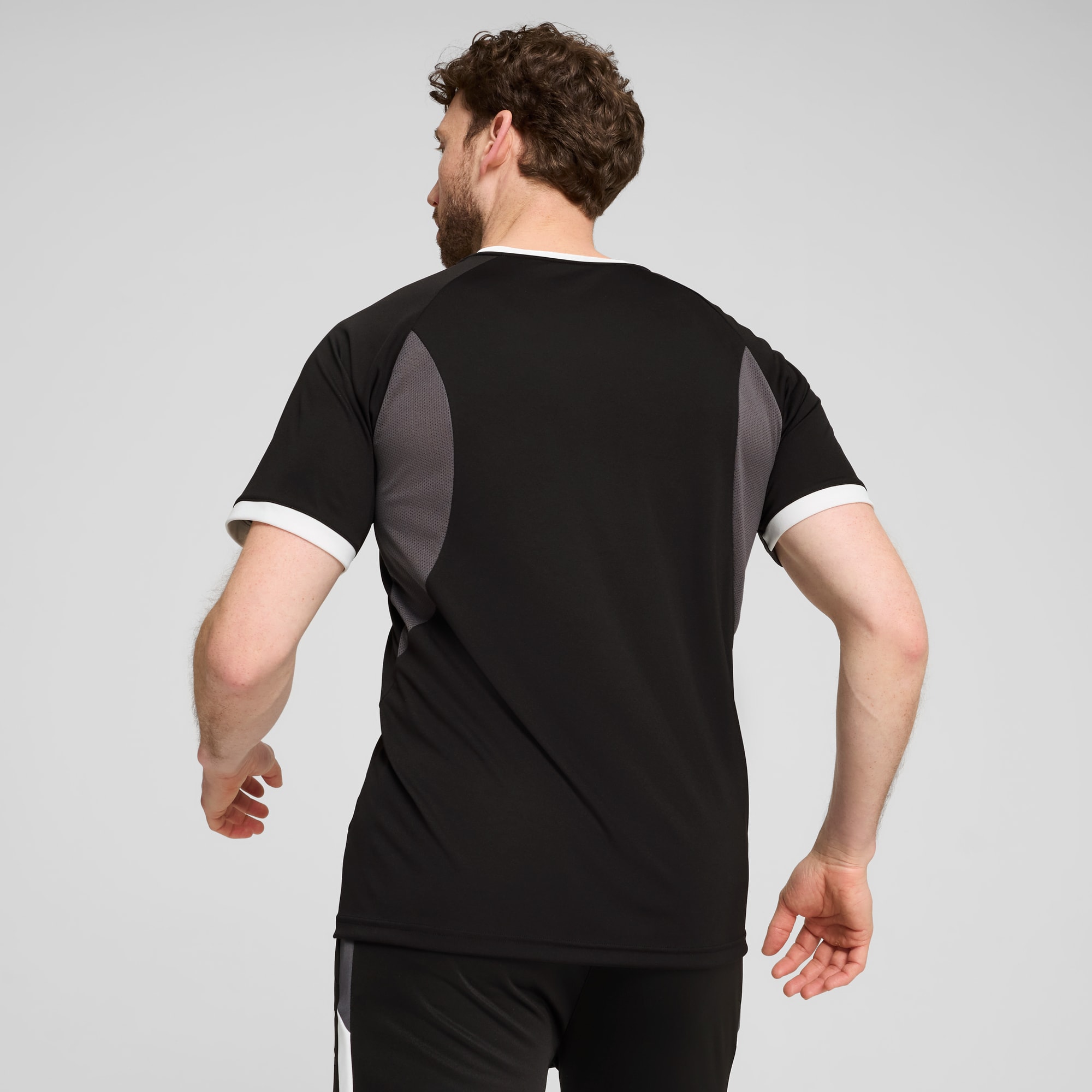 Ein Model mit dem Rücken zum Betrachter vor grauem Hintergrund, trägt ein schwarz-graues T-Shirt.