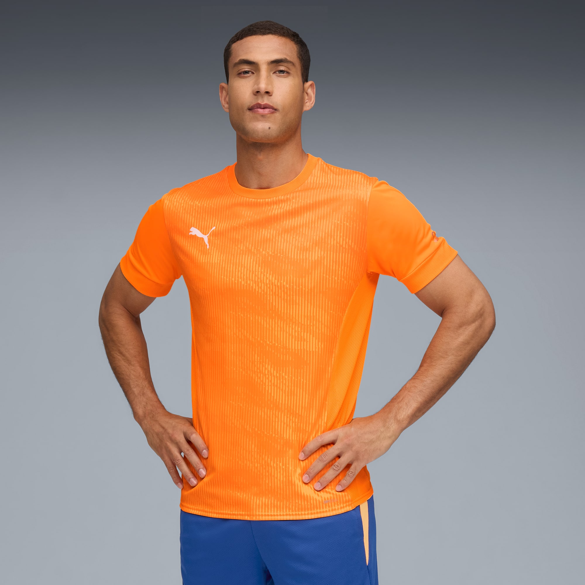 Un modello posa su sfondo grigio con maglietta arancione e pantaloncini blu.