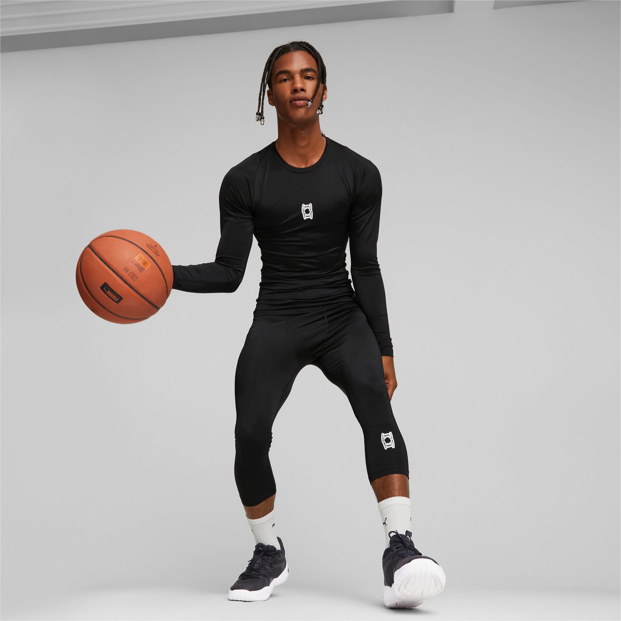 Sur fond gris, un mannequin en tenue de sport noire tient un ballon de basket, prêt à jouer.