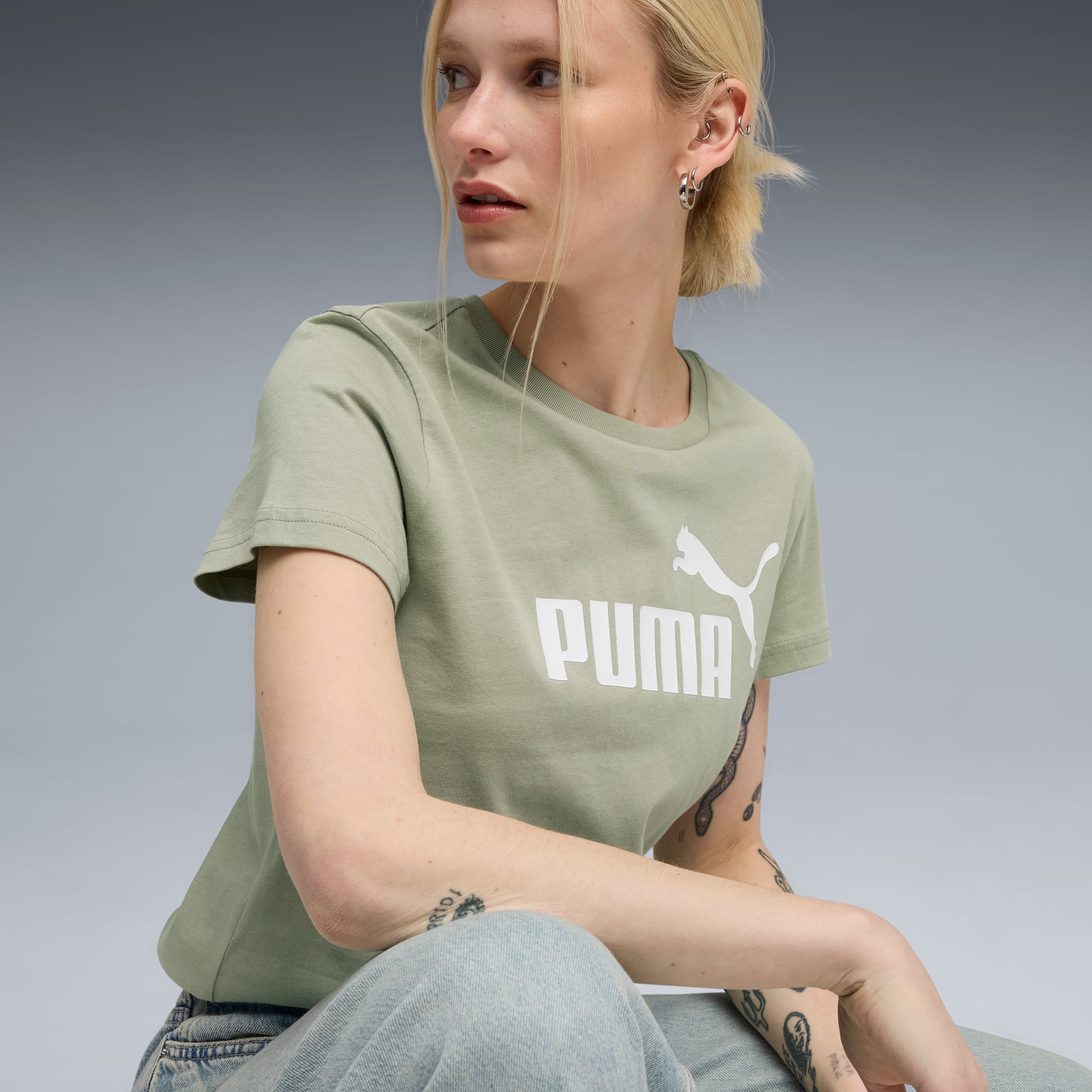 Een model poseert tegen een grijze achtergrond, met een groen Puma t-shirt en lichte jeans.