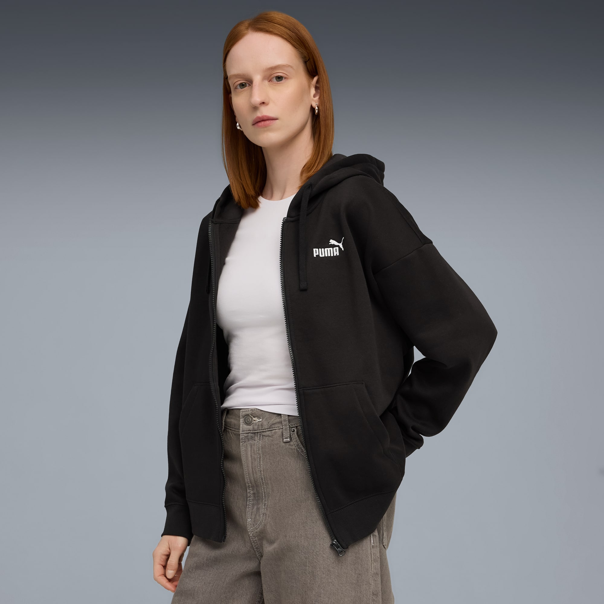 Un modelo con sudadera negra con cremallera sobre top blanco, fondo gris.