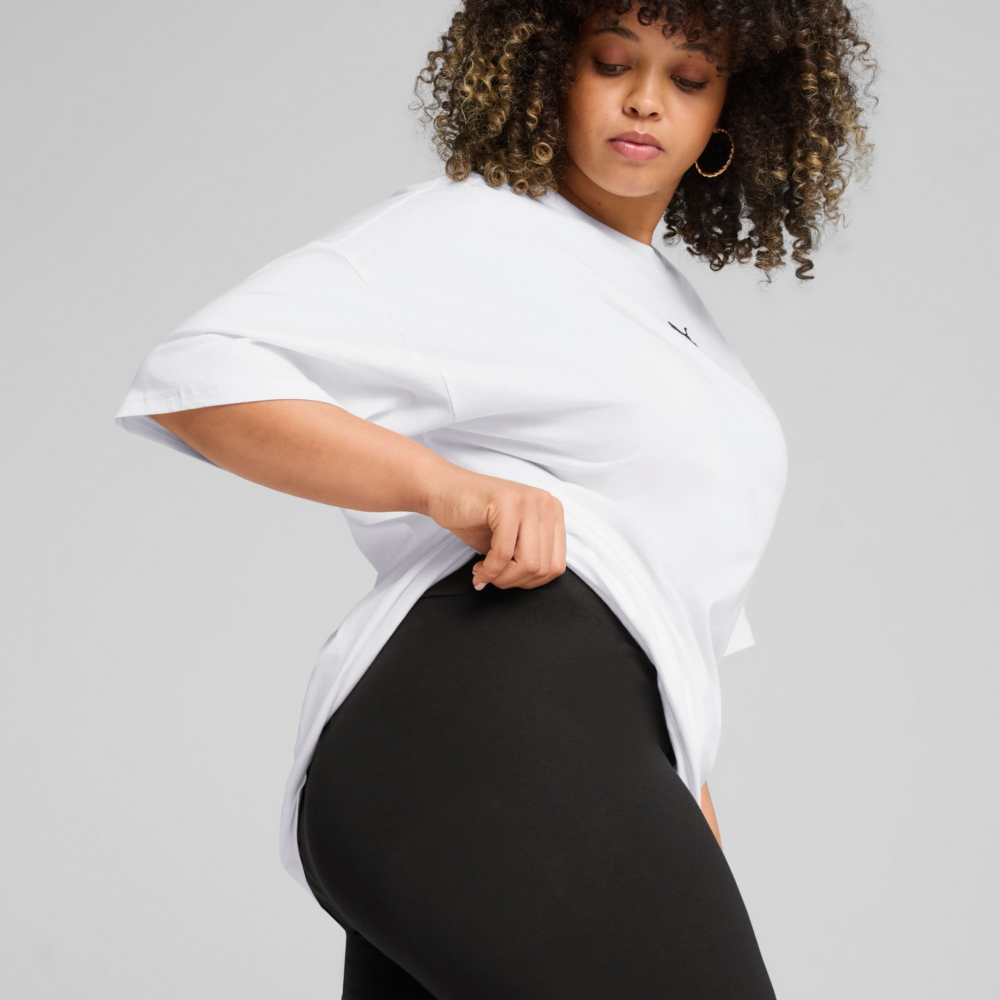 Sobre fondo gris, una modelo ajusta su camiseta blanca sobre unos leggings negros.