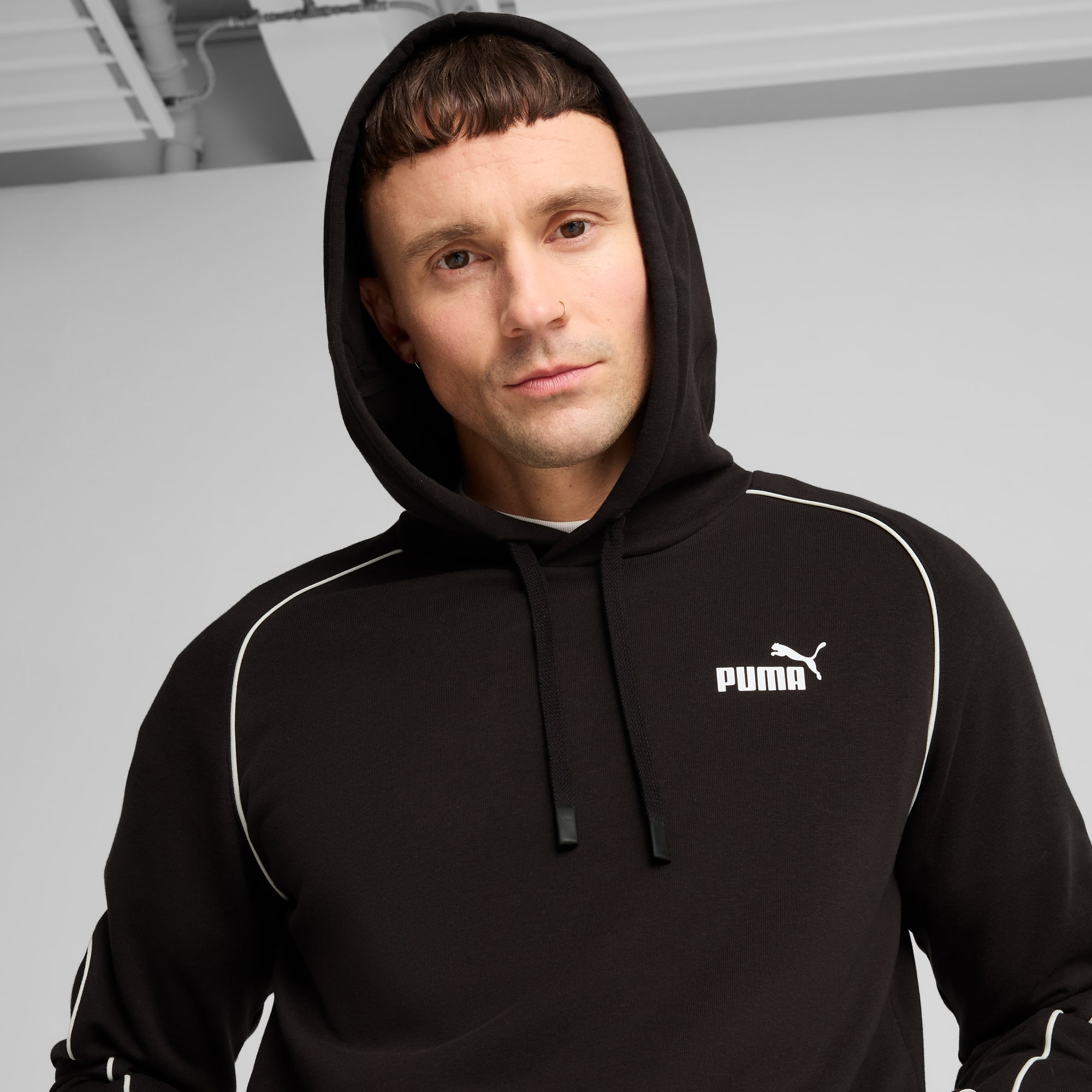 Un modèle pose sur fond gris, portant un sweat à capuche noir avec le logo Puma.
