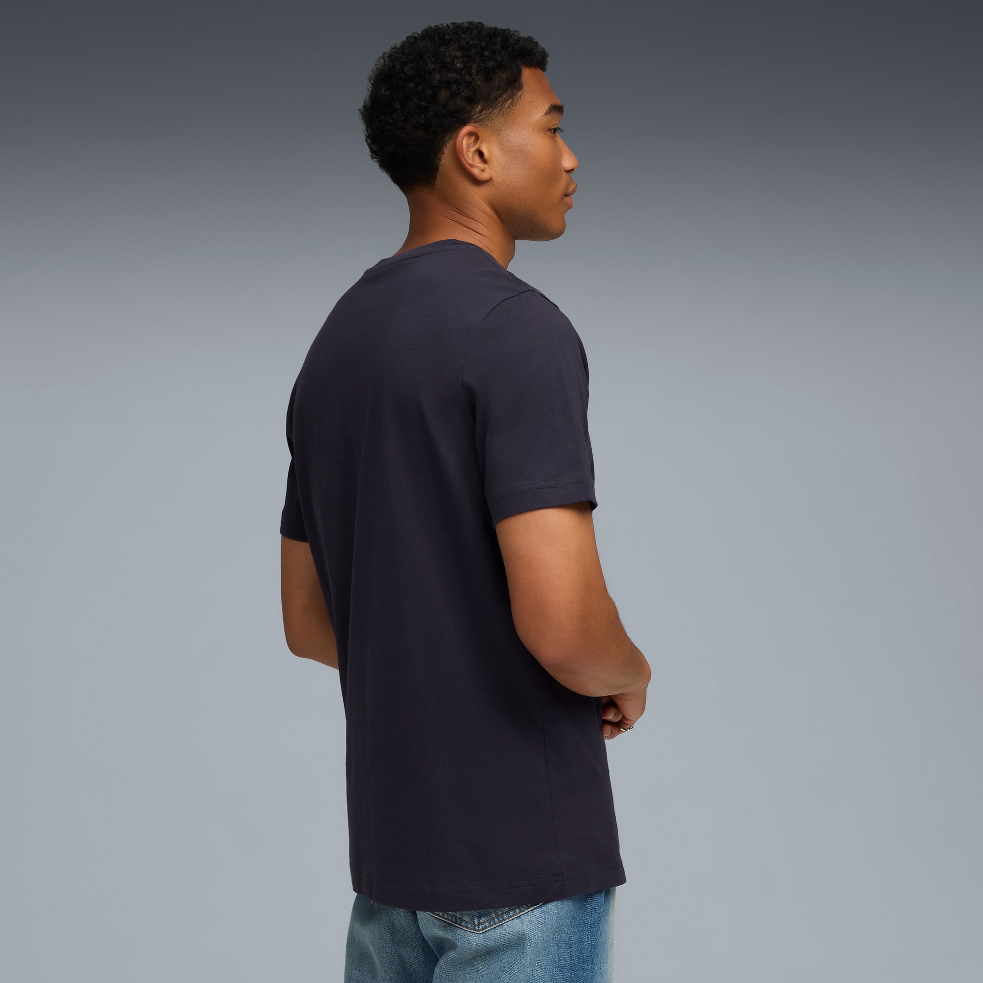 Vor grauem Hintergrund blickt ein Model in dunklem T-Shirt und Jeans zur Seite.