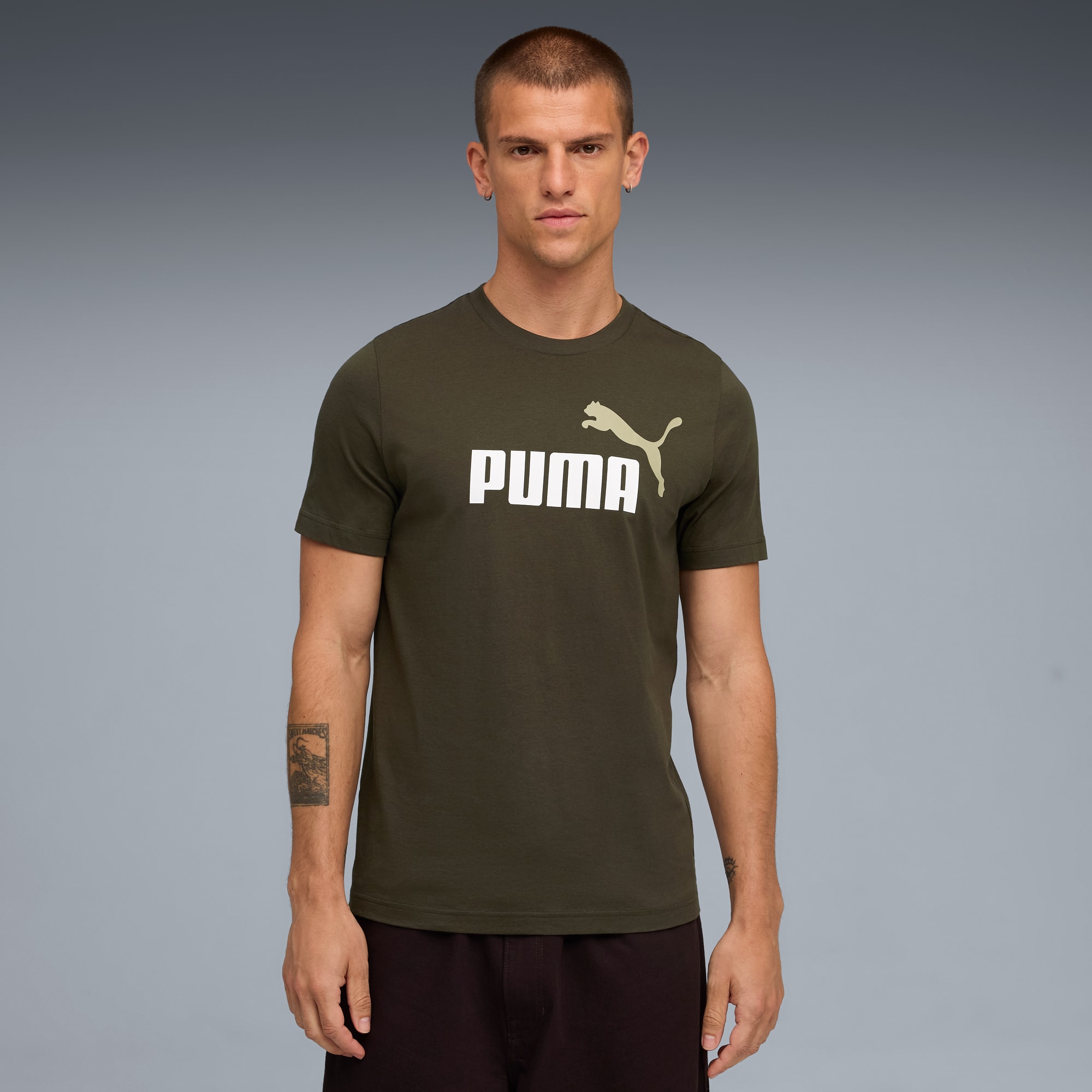 Un mannequin pose sur fond gris, portant un t-shirt olive avec un logo Puma blanc et un short foncé.