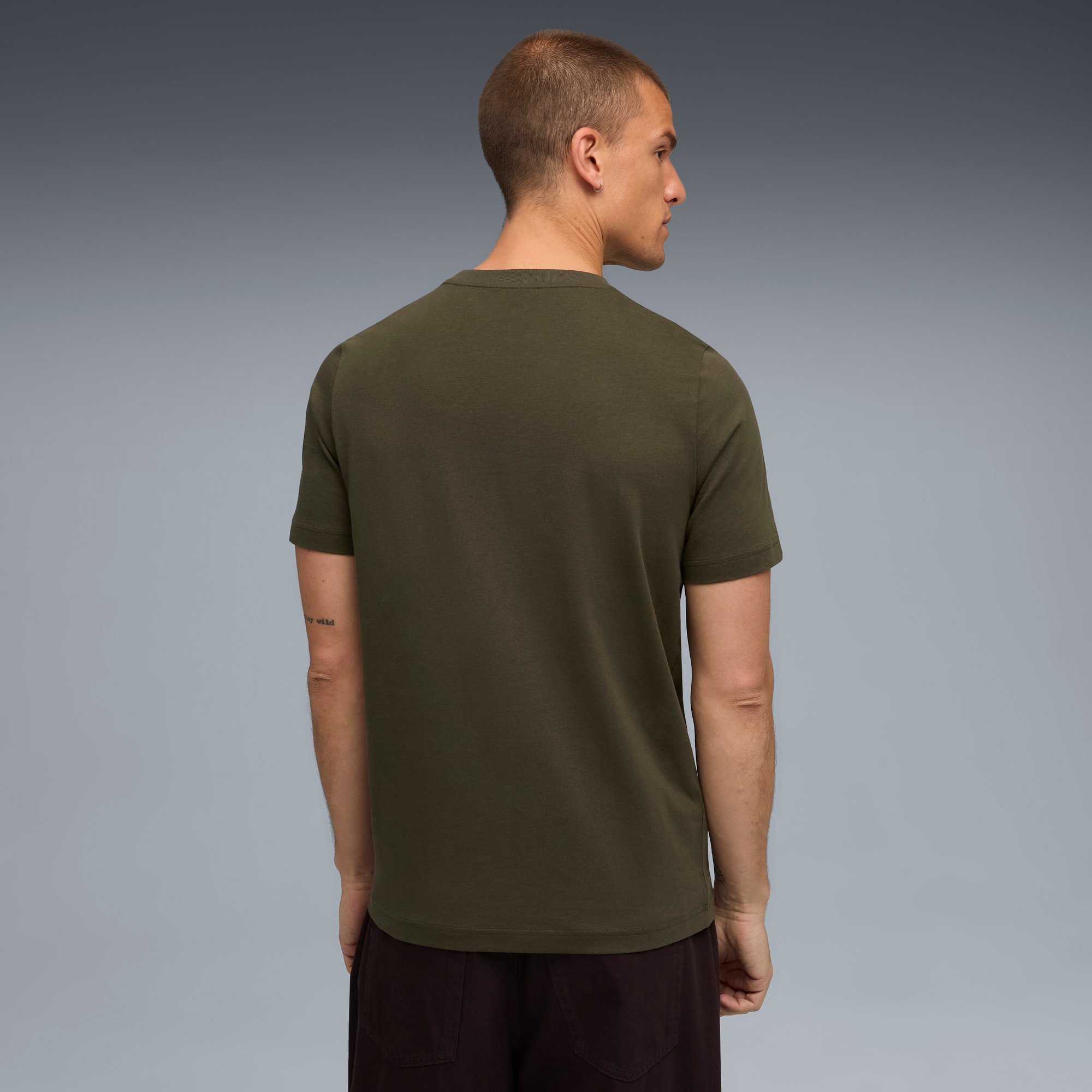 Un modèle, de dos, porte un t-shirt olive et un pantalon marron sur fond gris.