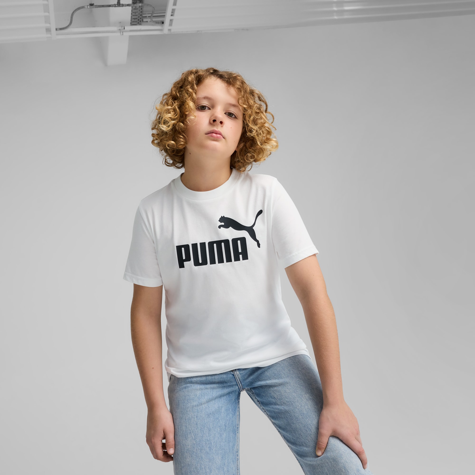 Un modello posa su sfondo grigio, indossando una t-shirt bianca Puma e jeans blu.