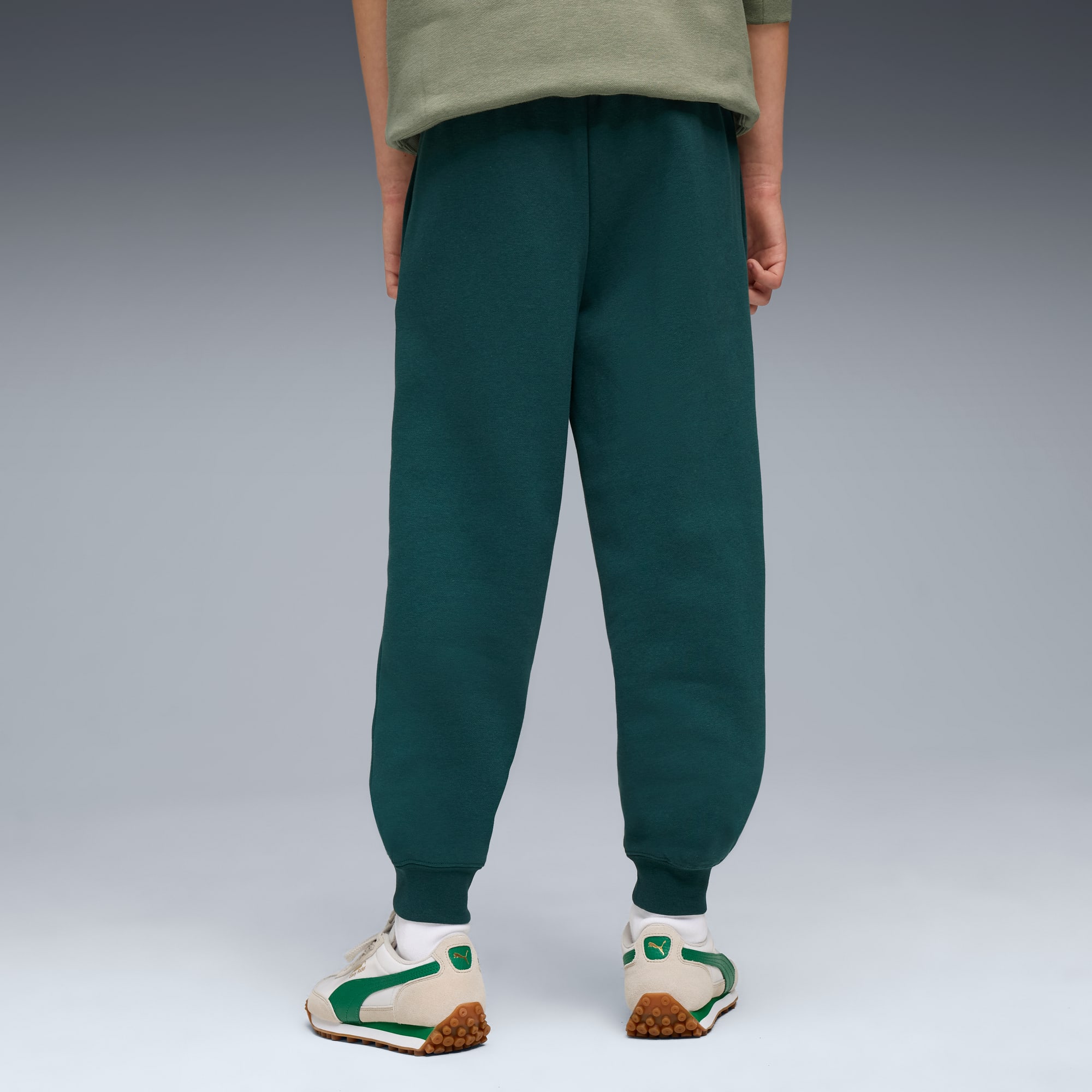 Ein Model vor grauem Hintergrund, trägt grüne Jogginghose und Turnschuhe mit Grün.