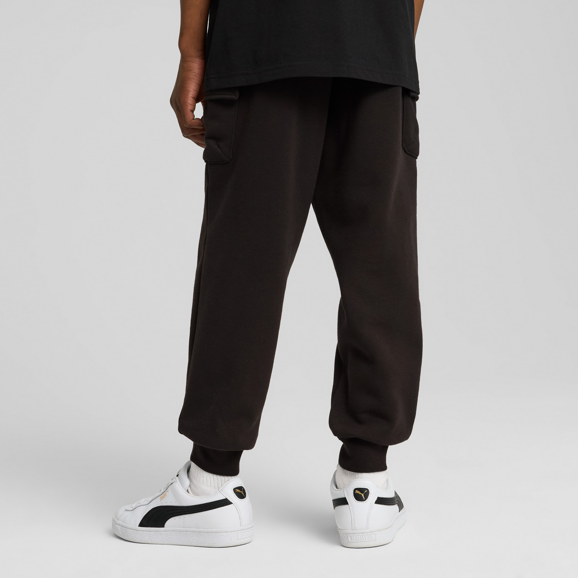 Vu de dos, un modèle porte un pantalon foncé et des baskets blanches sur fond gris.