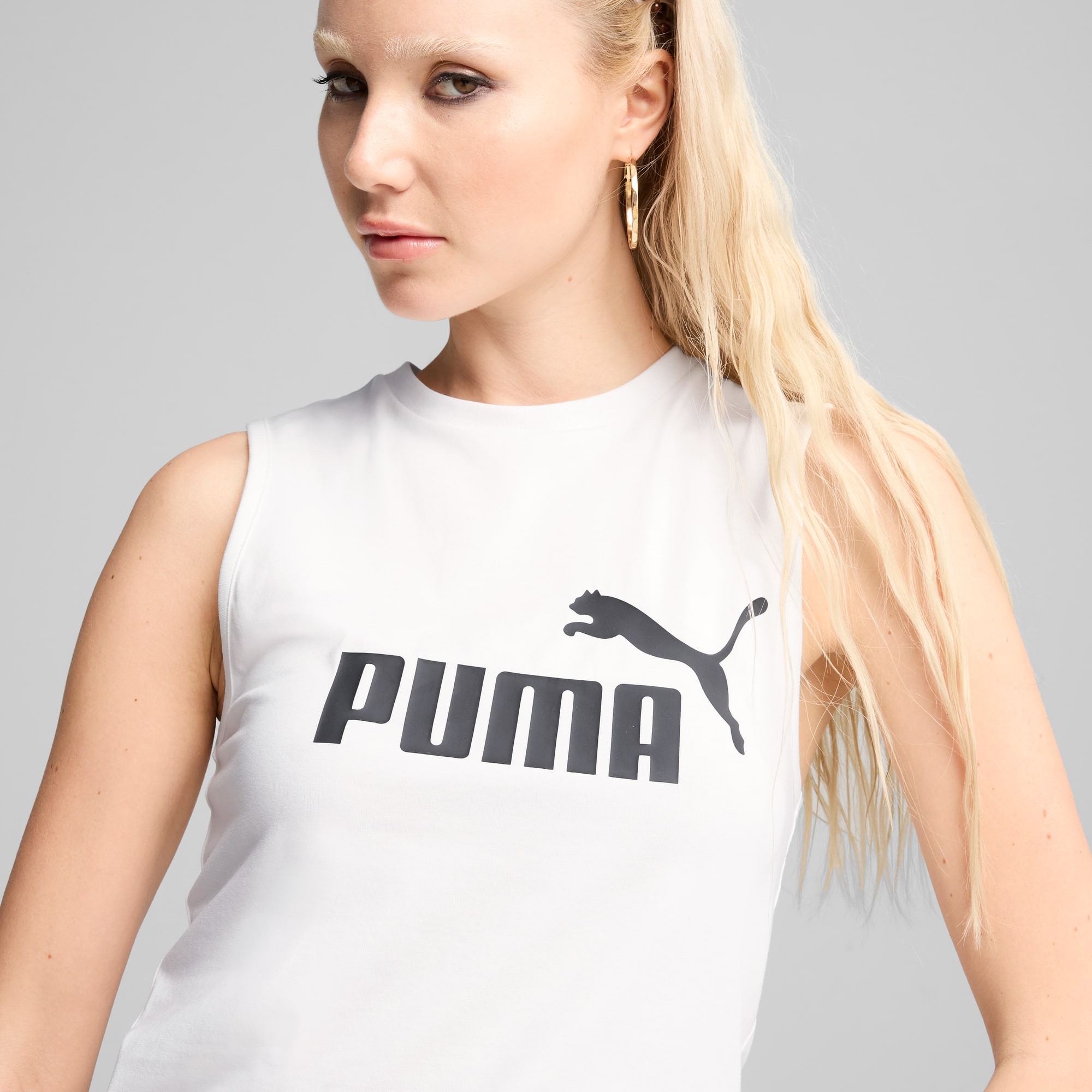 Una modella posa su sfondo grigio con una canotta bianca con il logo PUMA, guardando la fotocamera.