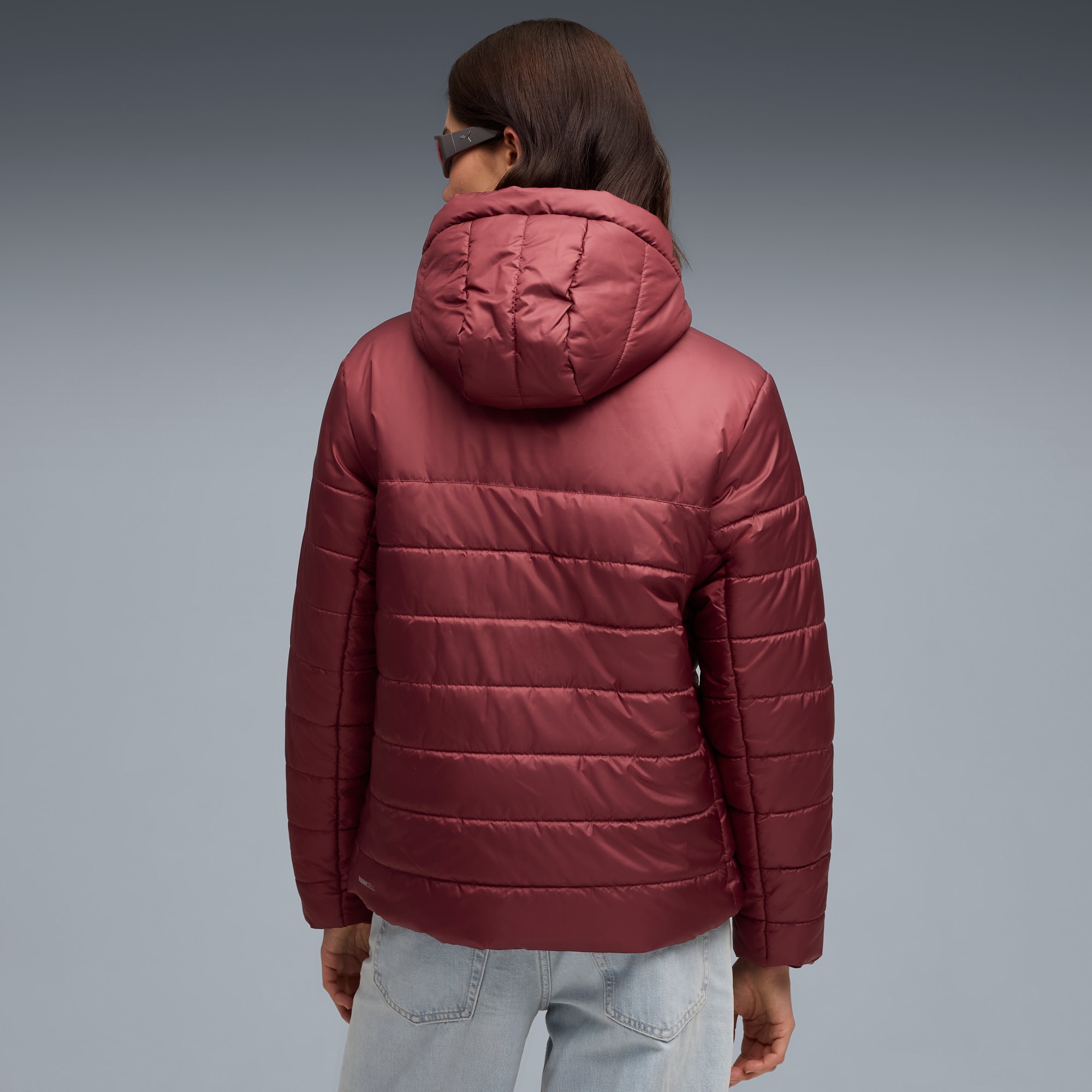 Een model met gewatteerde jas met capuchon op een grijze achtergrond, van achteren gezien.