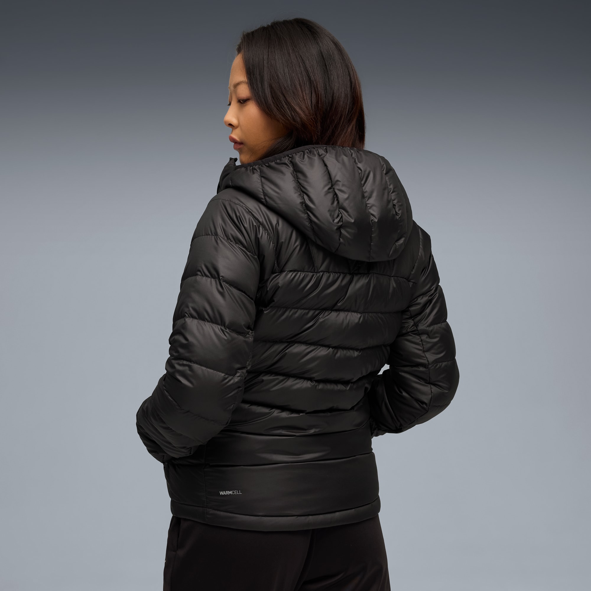 Sobre un fondo gris, una modelo viste una chaqueta acolchada negra con capucha.
