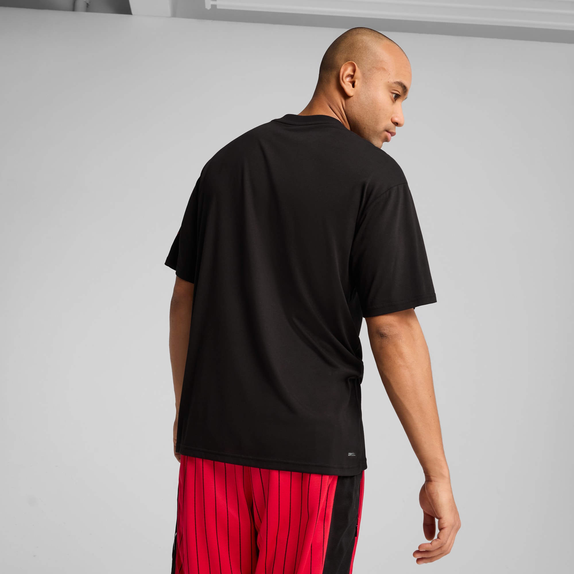 Een model voor een grijze achtergrond draagt een zwart T-shirt en rode short.