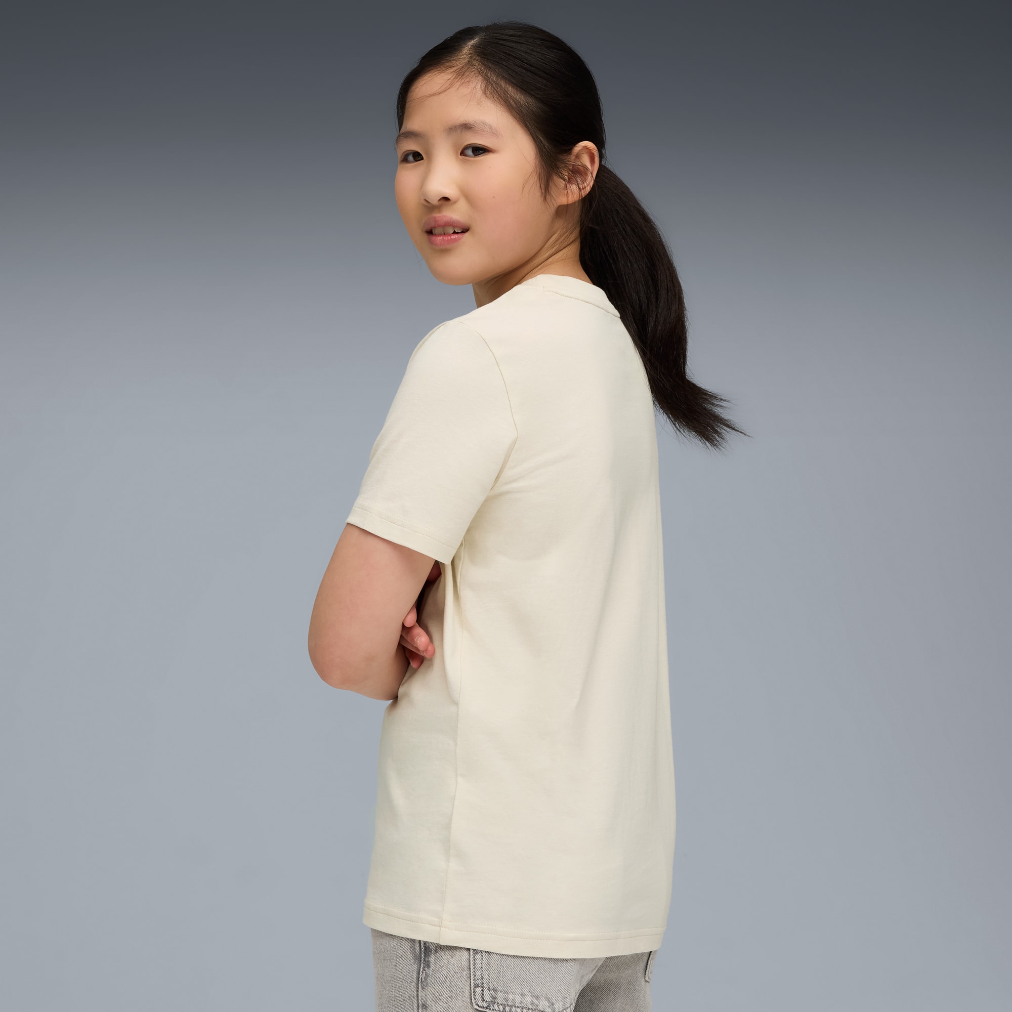 Una modella con le braccia incrociate, su sfondo grigio, indossa una t-shirt crema e pantaloncini grigi.